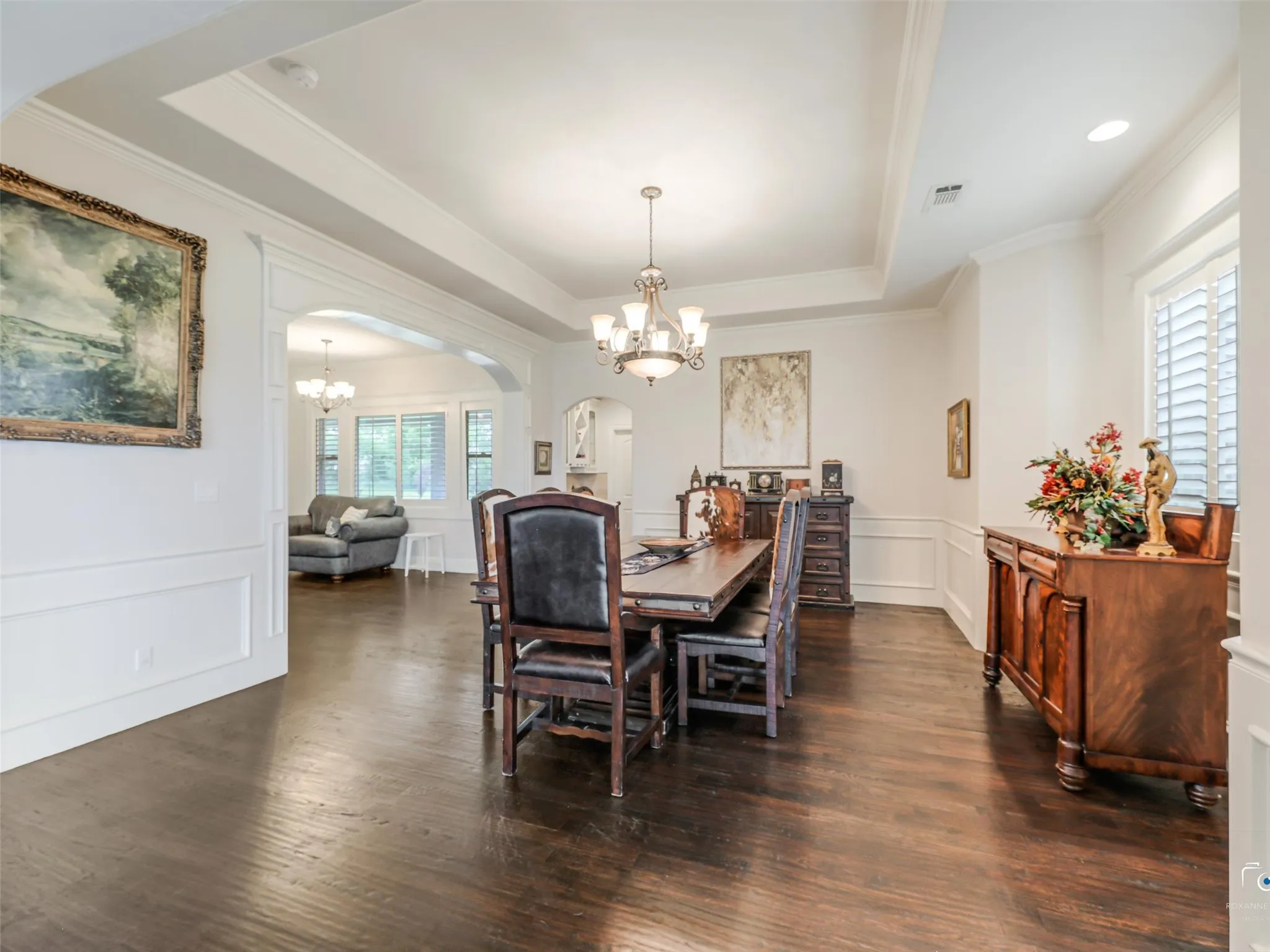 Formal dining area featuring dark wood-finish flooring, wainscoting, and a tray ceiling with a chandelier