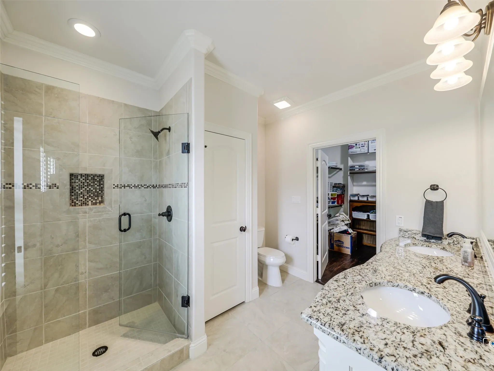 Spacious bathroom featuring a glass-enclosed shower with tile surround and mosaic accent, dual vanity with granite countertop and undermount sinks, bronze finish plumbing fixtures, and recessed lighting