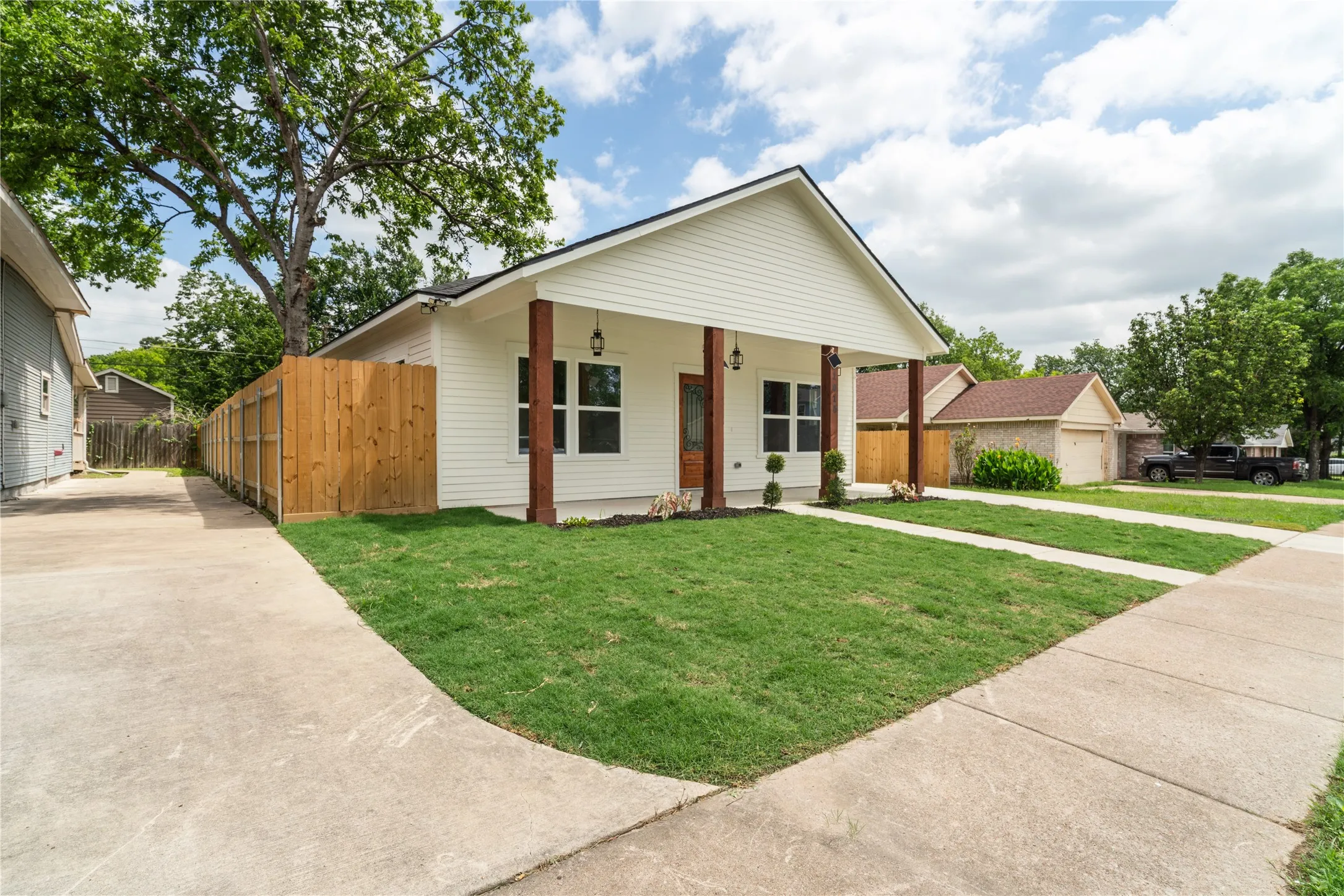 White siding residence featuring a covered front porch with dark wood columns, a manicured lawn, and a light wood privacy fence