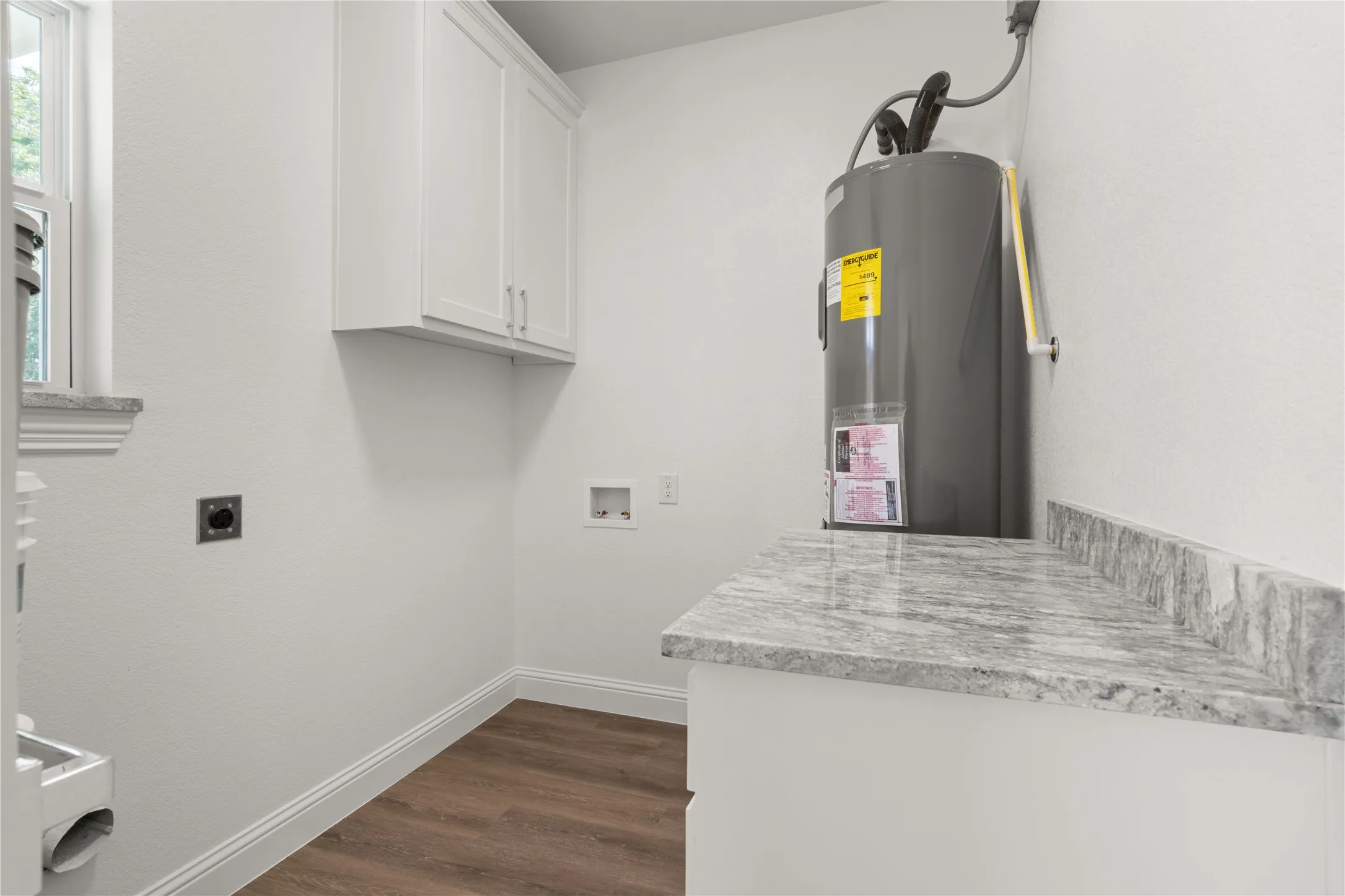 Laundry area featuring white shaker-style cabinetry, a gray patterned countertop, wood-finish flooring, and white baseboards