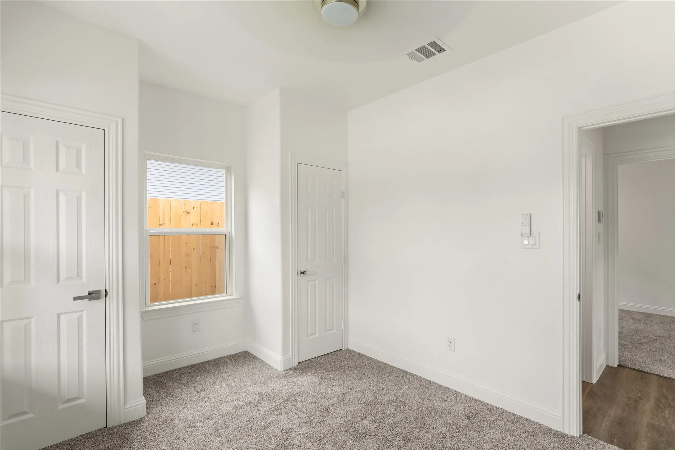 Neutral interior space with light gray carpet, white walls, and a single window featuring horizontal blinds