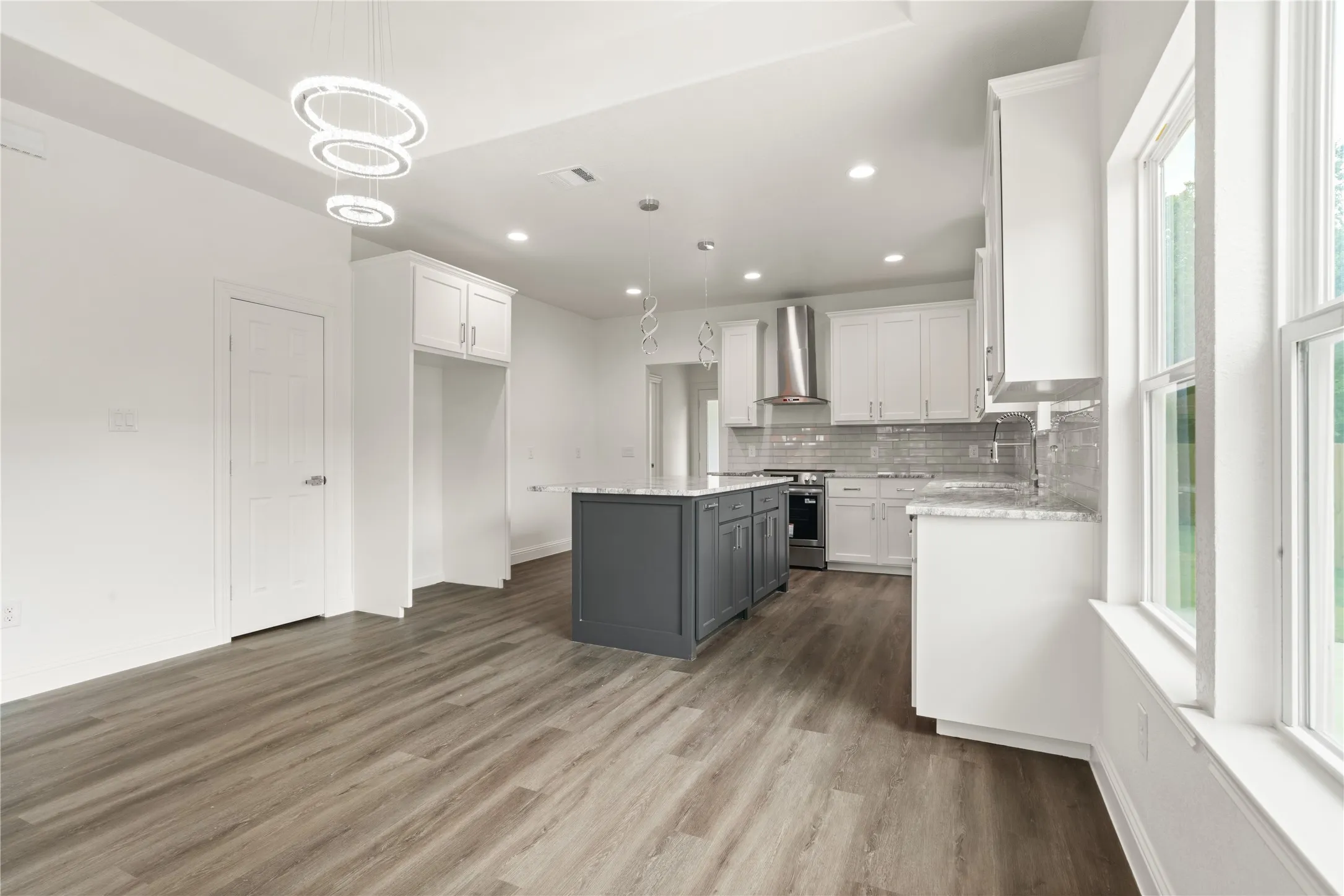 Contemporary kitchen featuring a gray island, white cabinetry, a subway tile backsplash, stainless steel range hood, and wood-finish flooring