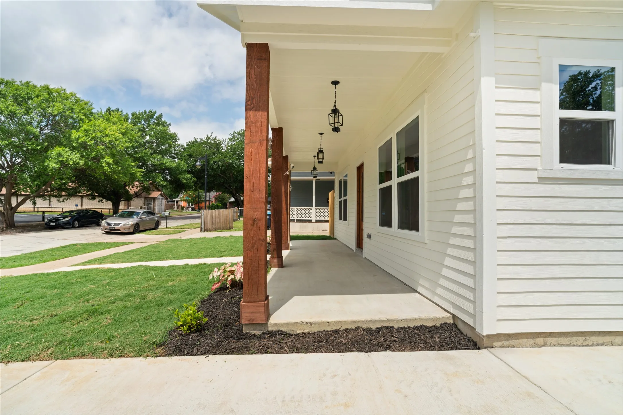 Inviting front porch featuring substantial wood-finish columns, pendant lighting, white horizontal siding, and multiple windows