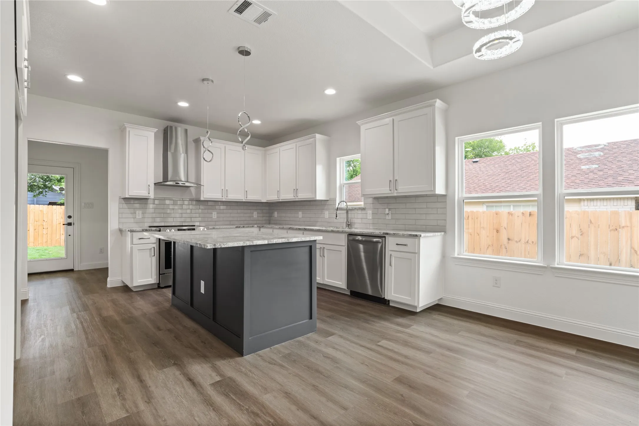 Open-concept kitchen featuring an island with a light-colored countertop, white cabinetry, stainless steel appliances, a subway tile backsplash, and recessed lighting