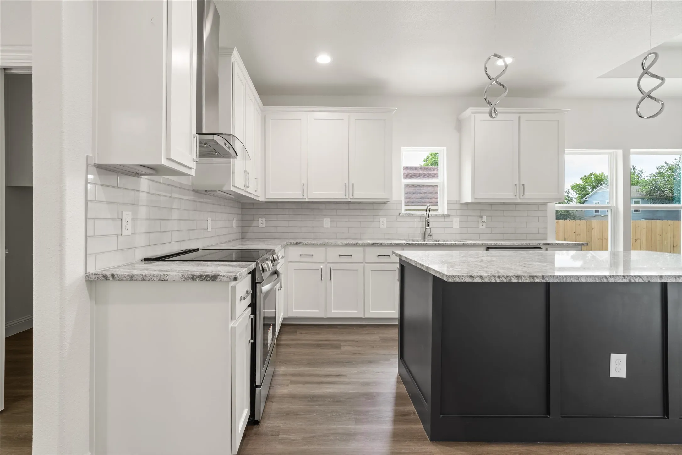 Kitchen featuring white shaker cabinetry, stainless steel appliances, light-toned countertops, subway tile backsplash, and a dark-toned island with integrated pendant lighting