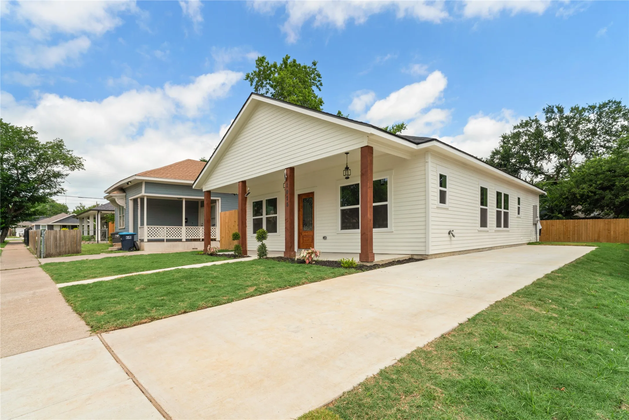 White siding exterior featuring a covered porch with natural wood columns, a concrete driveway, a manicured lawn, and a dark shingle roof