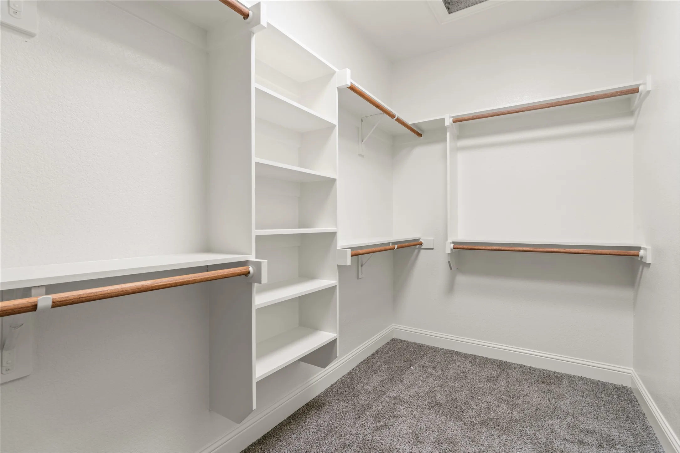 Walk-in closet featuring white built-in shelving, multiple hanging rods, and grey carpeting