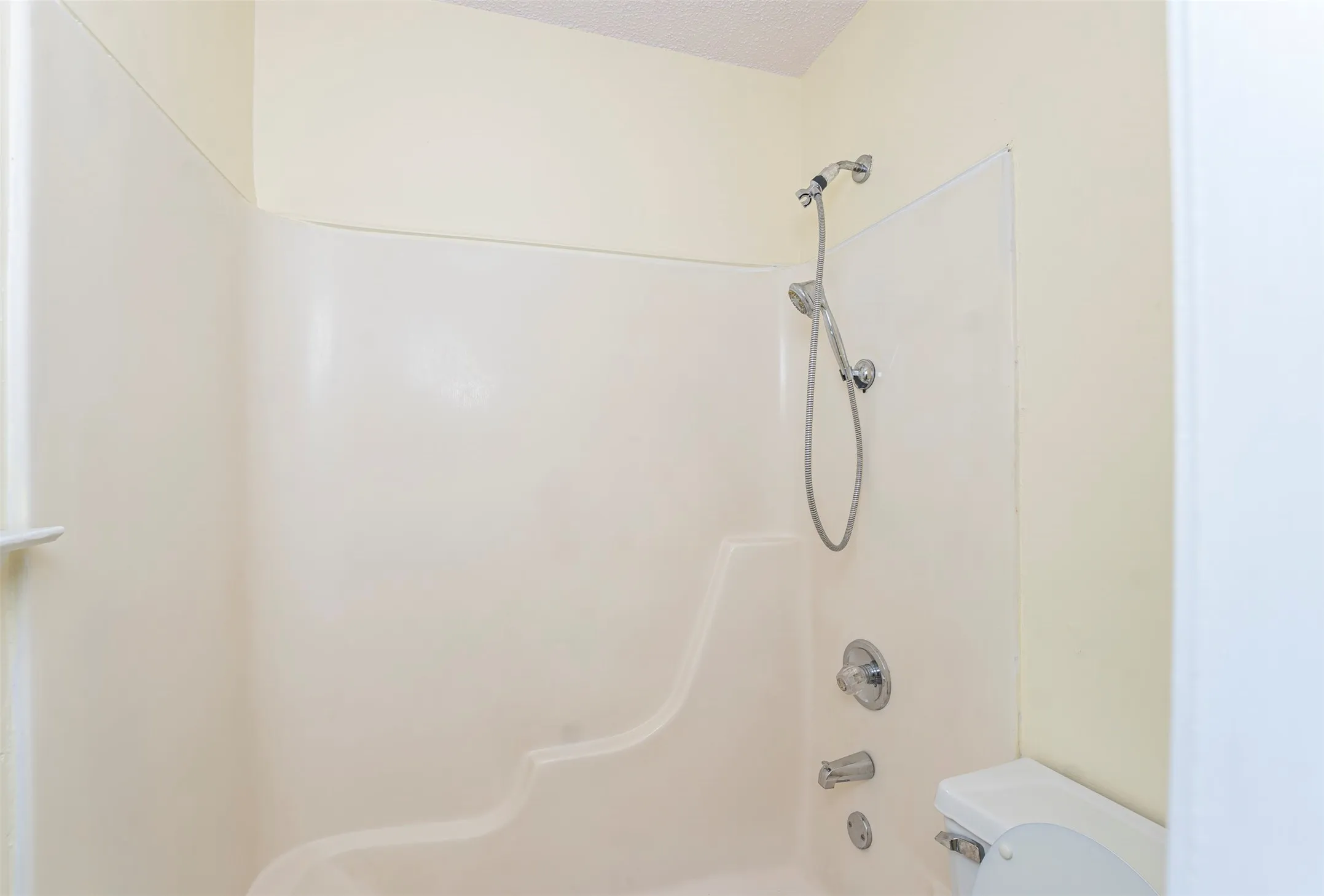 Bathroom featuring a white tub-shower combination unit with integrated shelving, chrome shower fixtures, and a white toilet