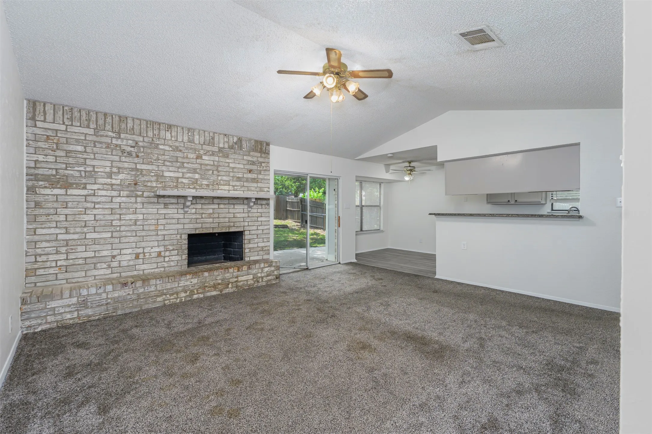 Living area featuring a textured brick fireplace, vaulted ceiling, and carpet flooring