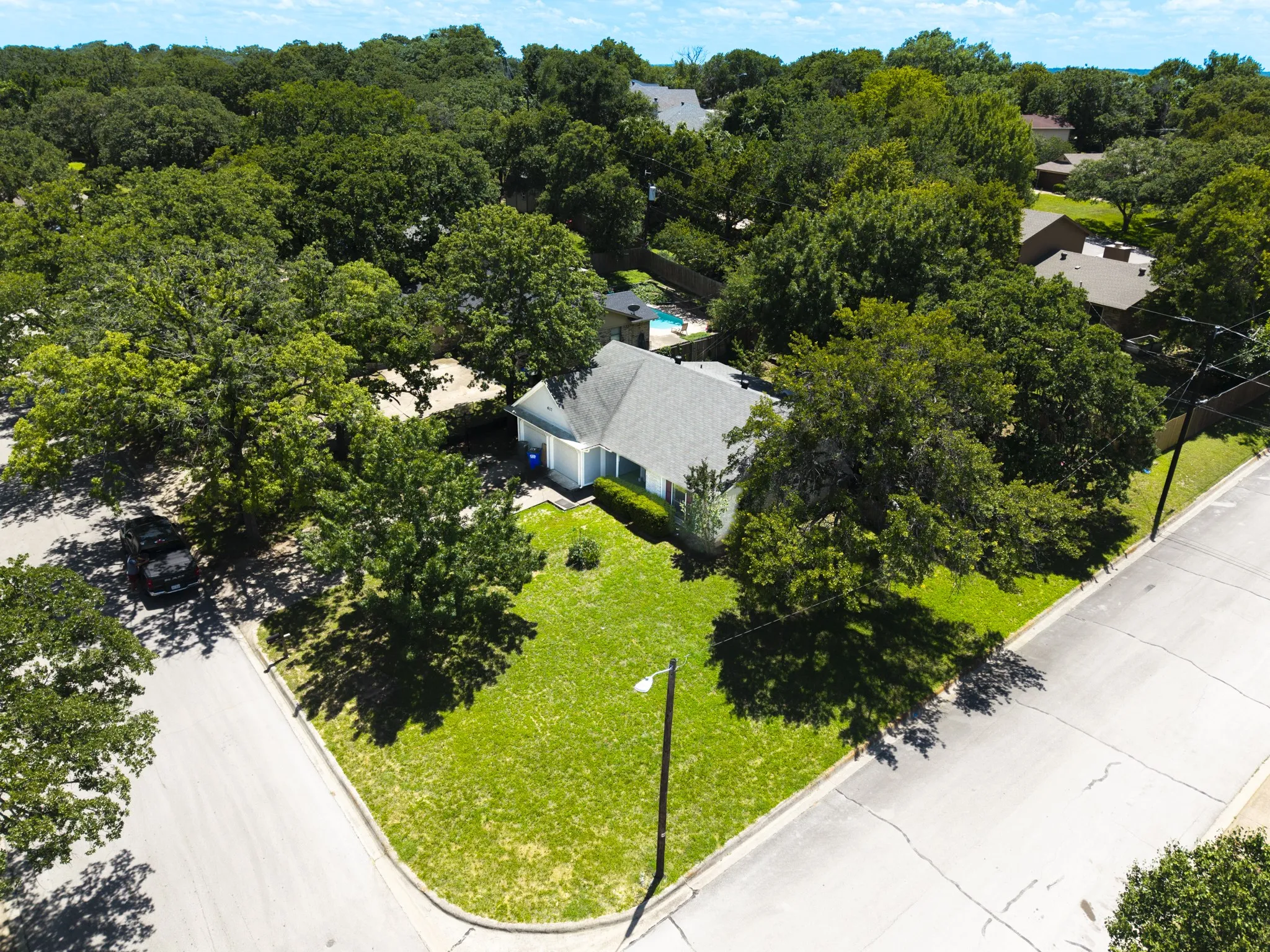 Corner lot property featuring a light-colored exterior, an angular roofline, and a vibrant green lawn
