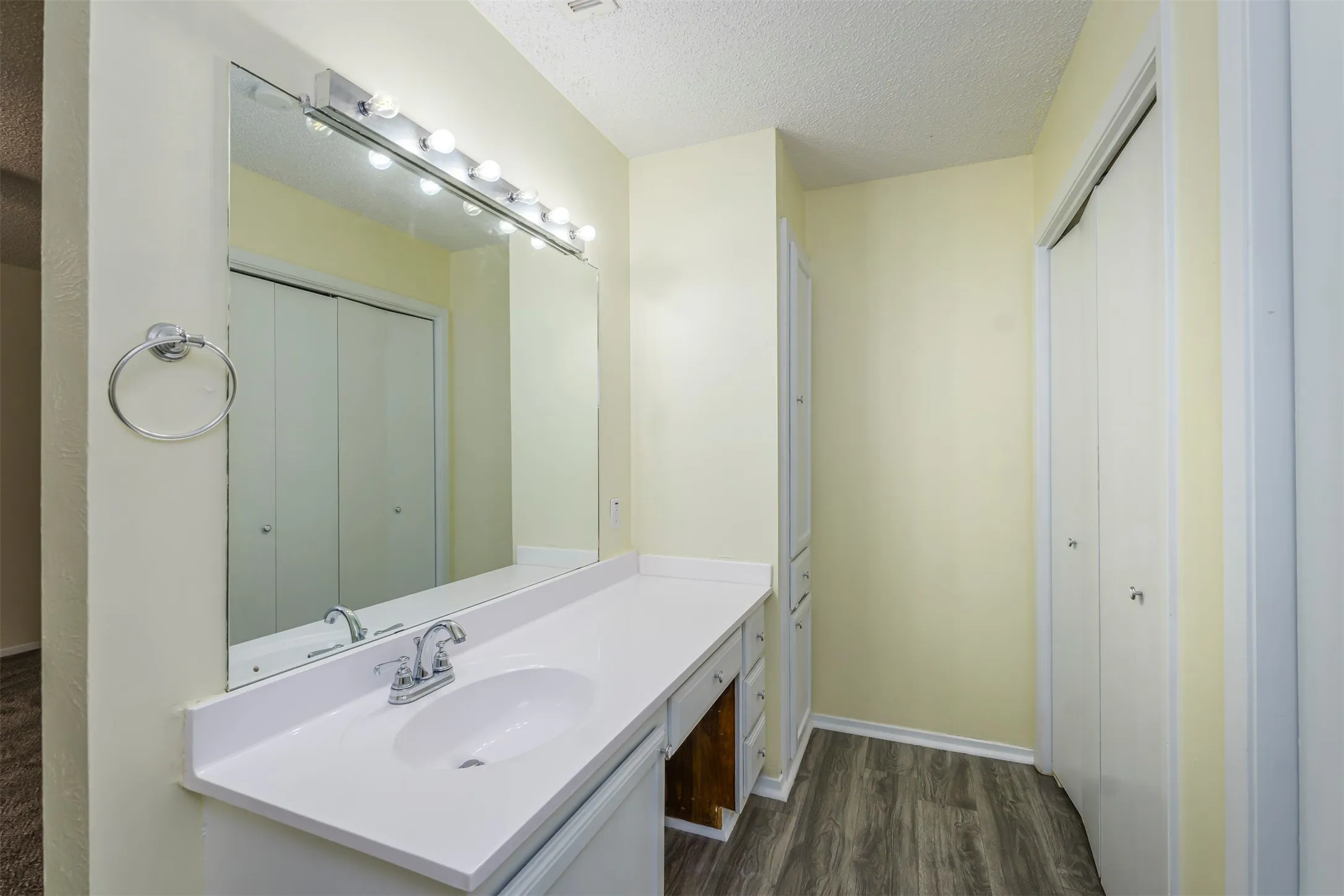 Bathroom vanity featuring a large mirror with strip lighting, a white countertop with an integrated sink, and wood-finish flooring