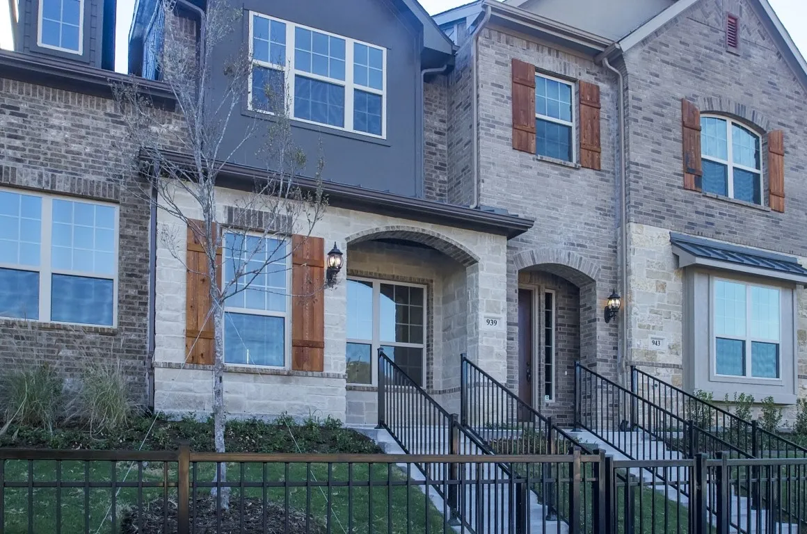 Brick and stone facade townhomes featuring arched entryways, dark framed windows, wood-finish shutters, and black wrought iron fencing