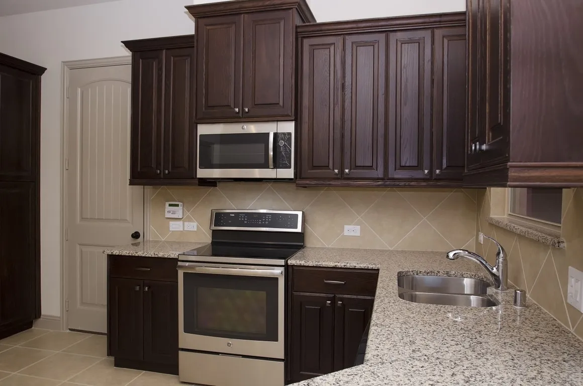 Kitchen featuring dark wood-finish cabinetry, stainless steel appliances, speckled stone countertops, a stainless steel sink, and a tiled backsplash