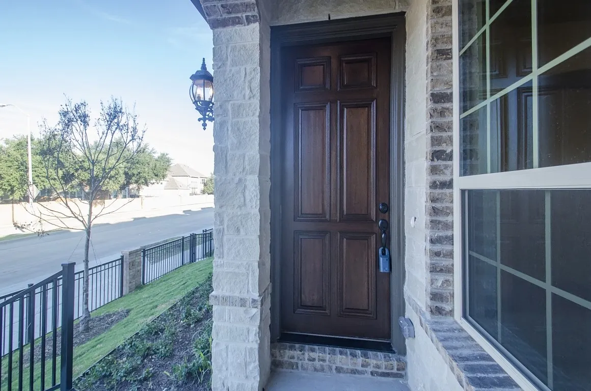 Panelized wood-finish front door with an integrated window, framed by stone veneer columns and brick accents