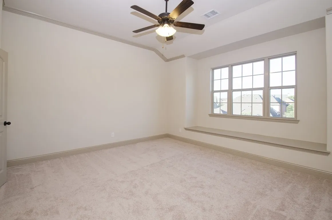 Spacious room featuring a three-panel window with grid design, a built-in window bench, light-toned carpeting, and a ceiling fan with integrated lighting