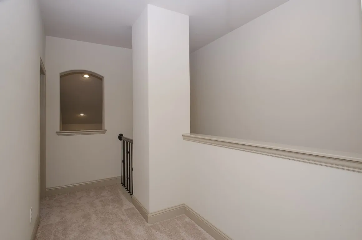 Upper-level hallway featuring a decorative wall niche with recessed lighting, wrought iron balustrade, and neutral-toned carpeting