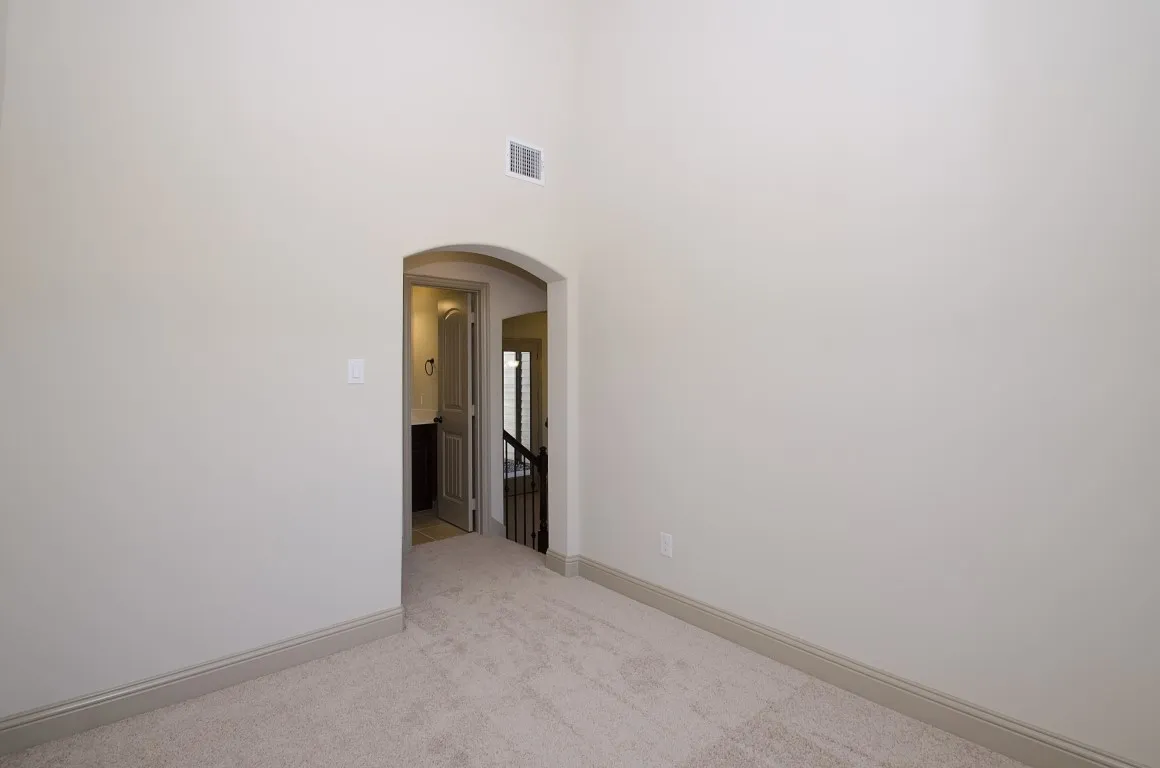 Carpeted room featuring an arched doorway, high ceilings, light-toned walls, and baseboard trim