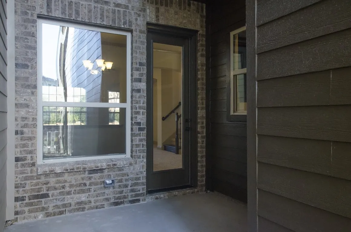 Exterior patio featuring a neutral concrete surface, brick facade, dark horizontal siding, and a glass-paneled entry door