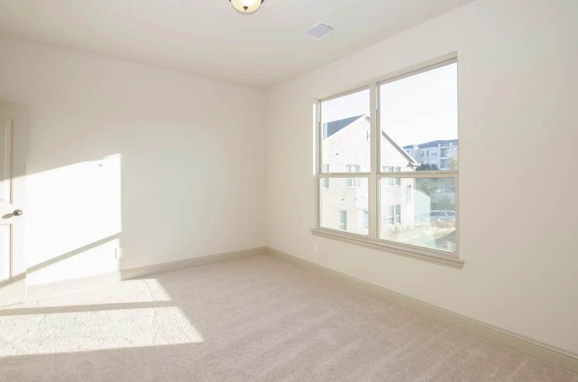 Carpeted room featuring a large window with white trim, a recessed ceiling vent, and a flush mount ceiling light