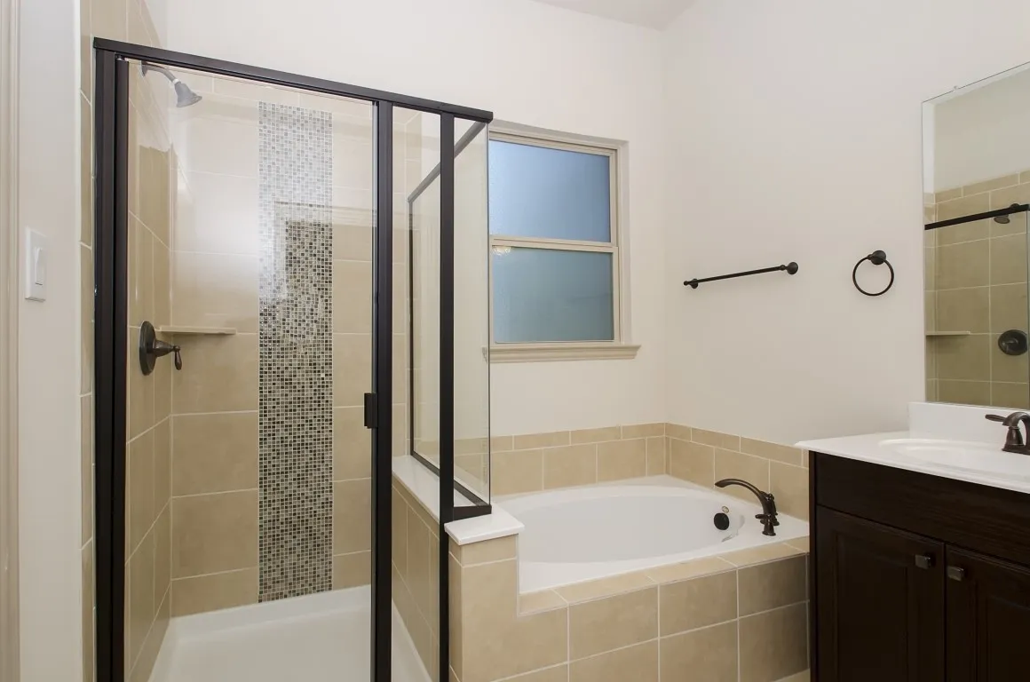 Bathroom featuring a tiled soaking tub, a separate shower with a mosaic tile accent, and a dark wood-finish vanity with a single sink