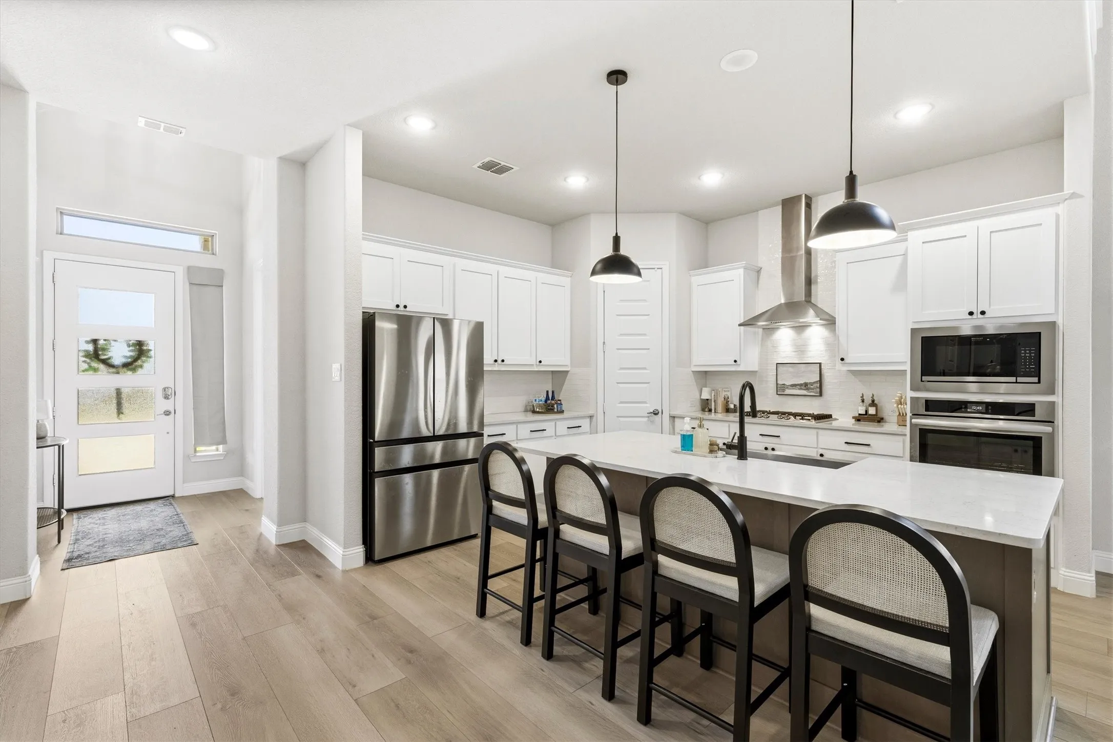 Contemporary kitchen featuring an oversized island with seating, stainless steel appliances, white cabinetry, and recessed lighting