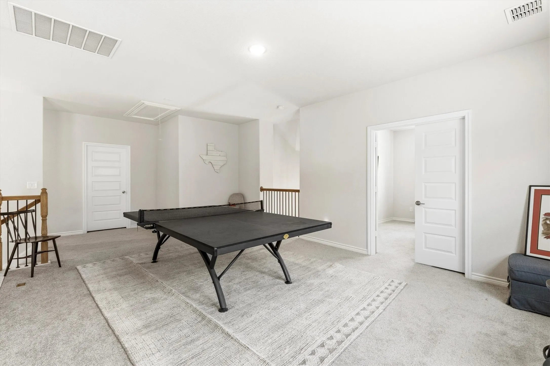 Spacious upstairs area featuring light gray carpeting, neutral wall tones, white five-panel interior doors, and a wood banister with dark spindles