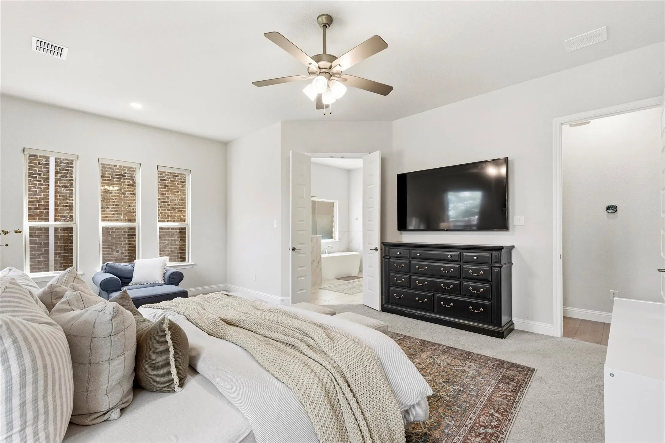 Carpeted bedroom with a ceiling fan, recessed lighting, and three windows offering exterior brickwork