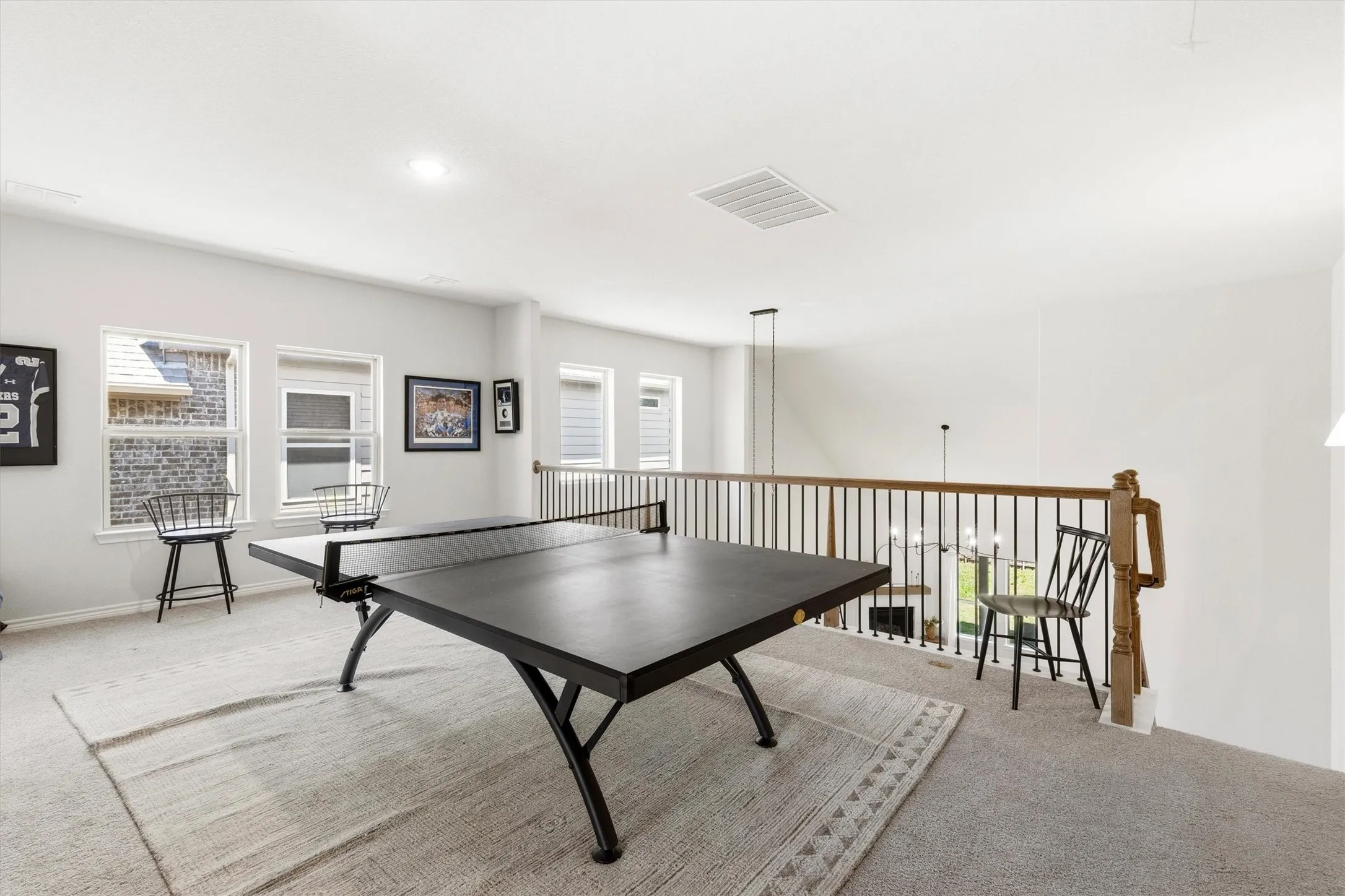 Open loft space featuring light gray carpeting, multiple windows, and a wood railing with black metal spindles overlooking the floor below