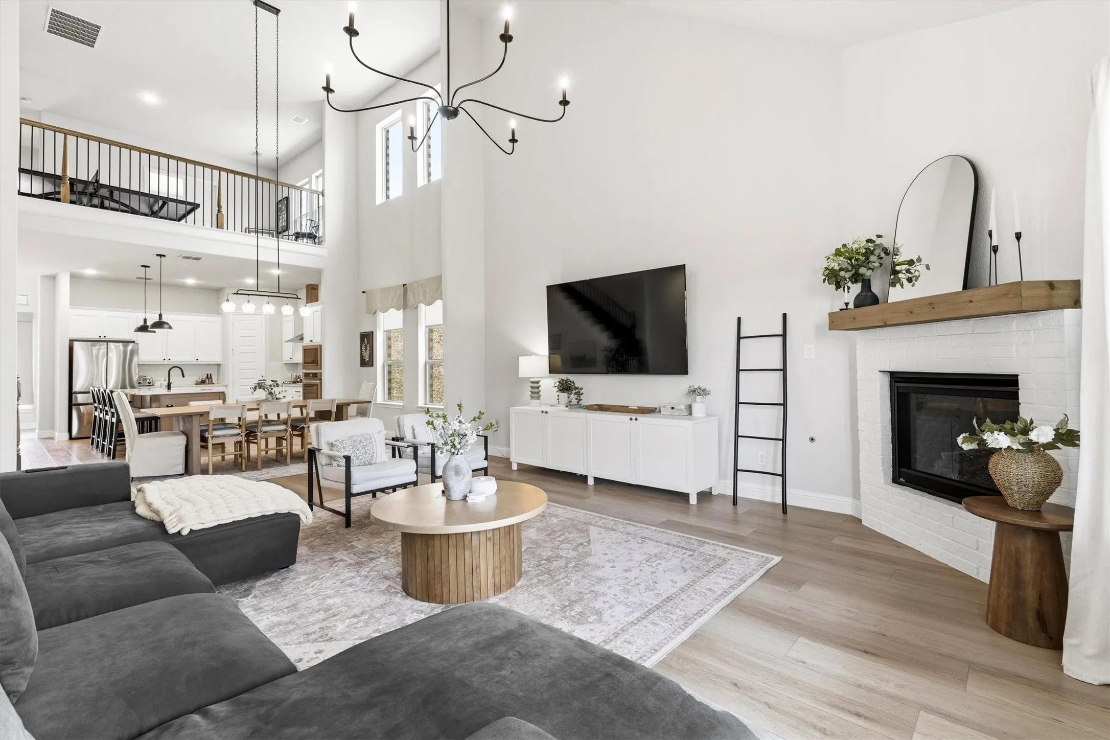 Vaulted living area featuring light wood-finish flooring and a white brick fireplace with a wood mantle