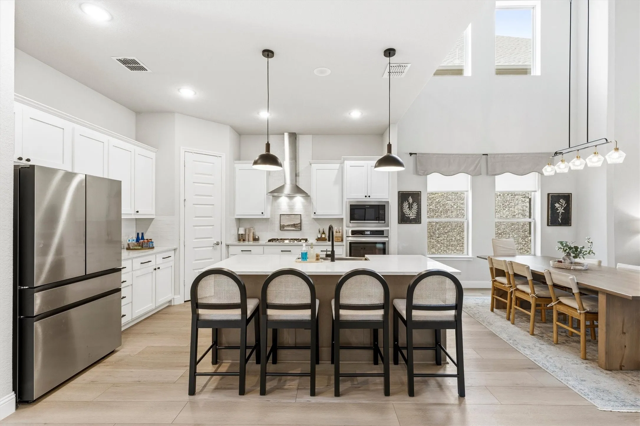 Open-concept kitchen and dining area featuring light wood-finish flooring, a central island with integrated seating, white shaker-style cabinetry, and stainless steel appliances