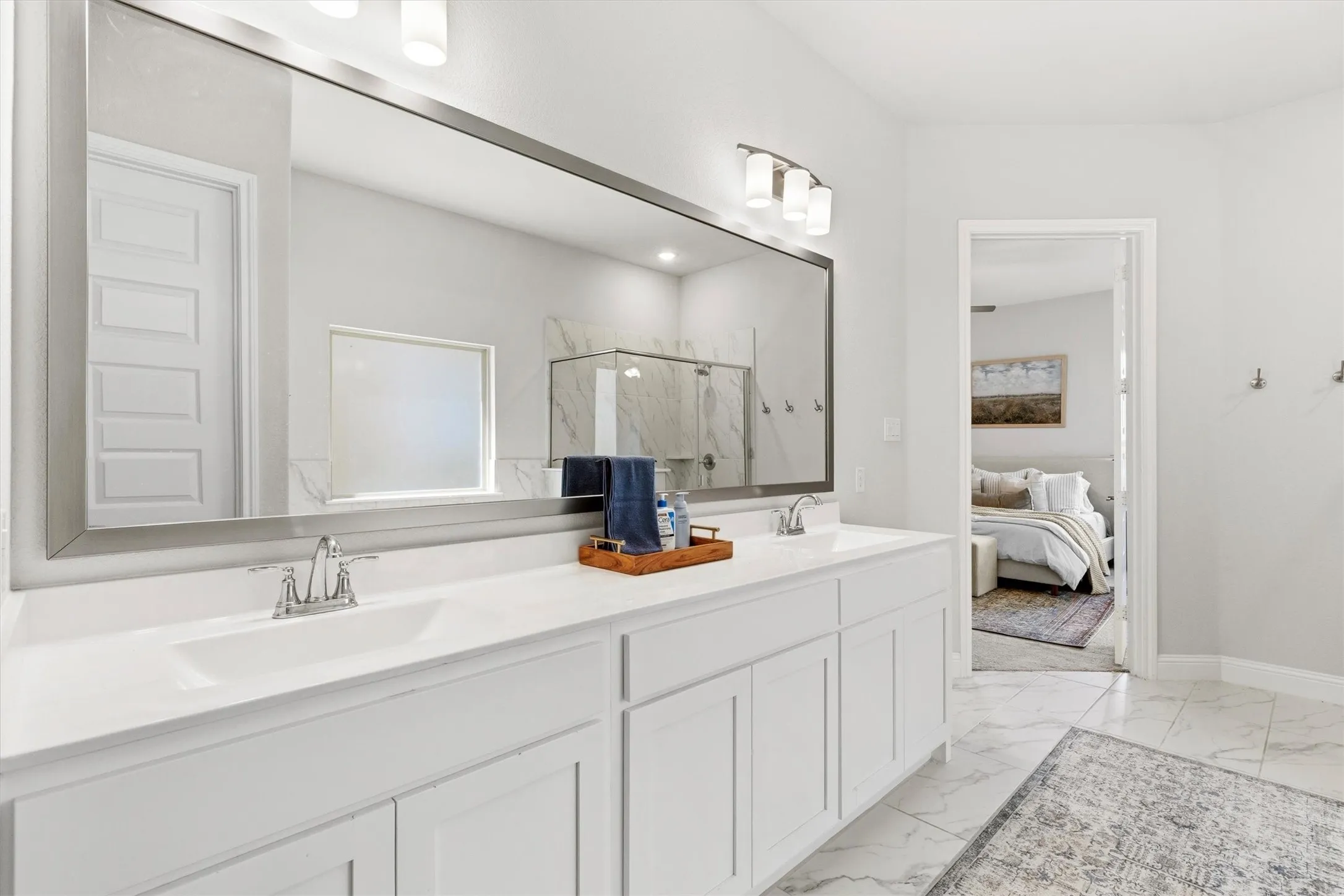 Dual vanity with white cabinetry and integrated sinks, complemented by a large framed mirror and a three-light fixture