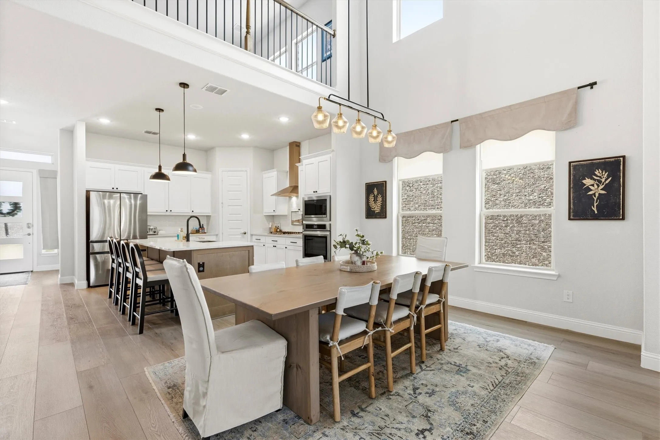 Open-concept living area featuring high ceilings, wood-finish flooring, a modern kitchen with a large island, stainless steel appliances, and a second-story interior balcony