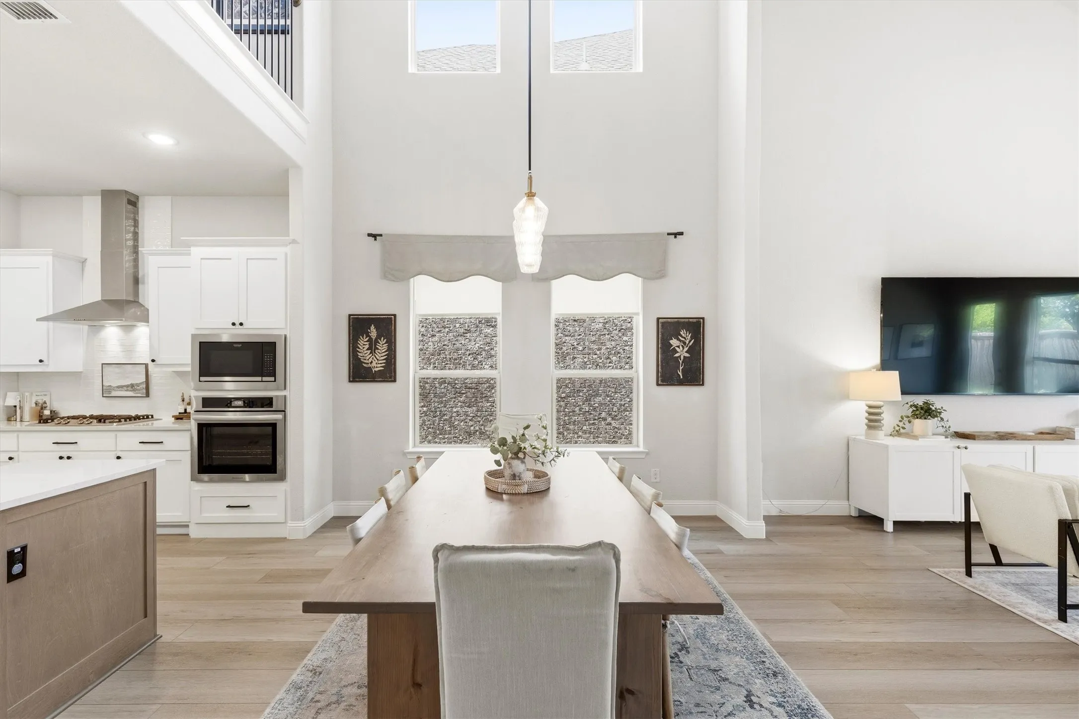 Open-concept interior featuring light wood-finish flooring, a double-height ceiling, and a contemporary pendant light fixture