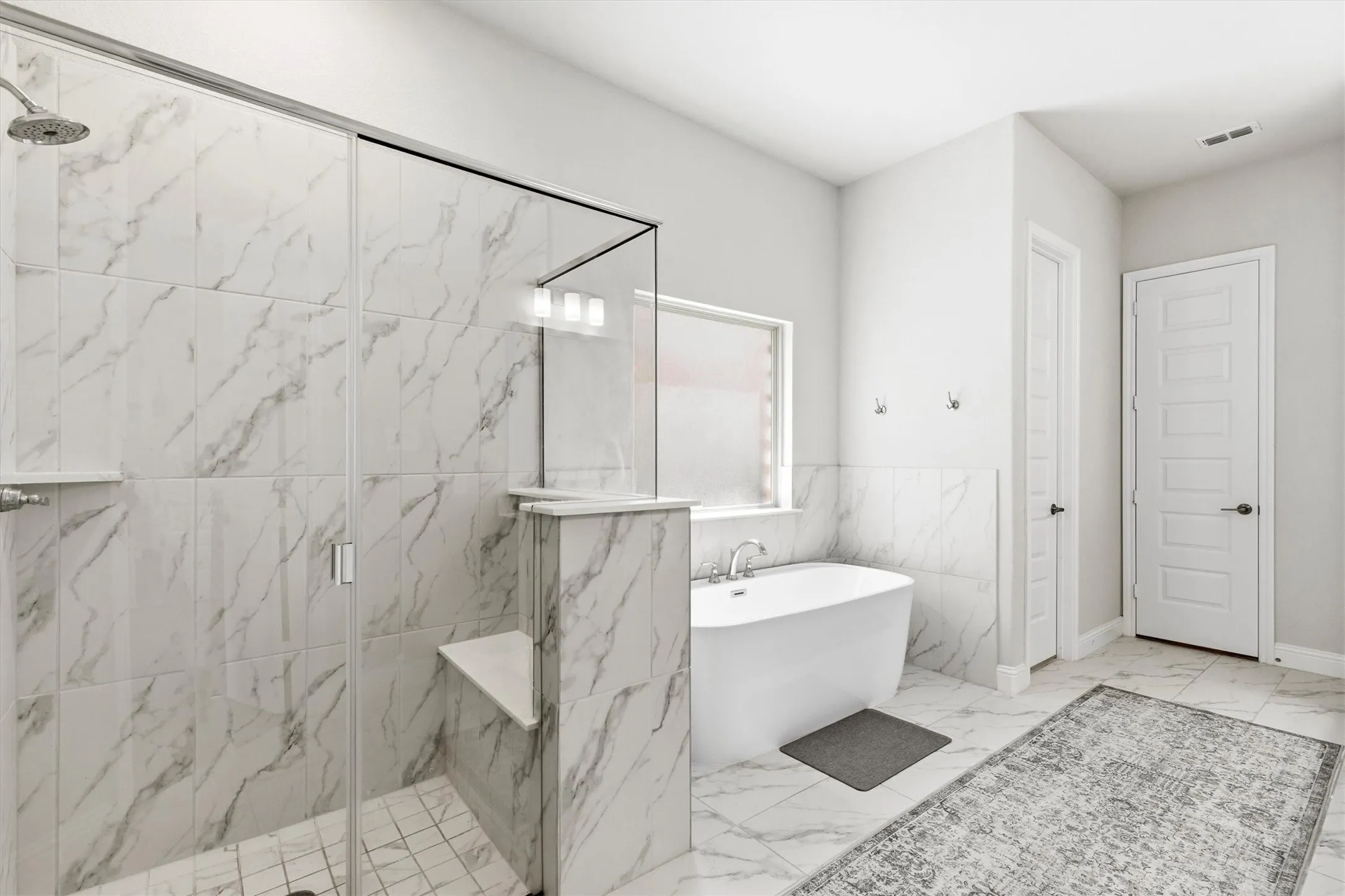 Spacious bathroom featuring a frameless glass shower enclosure, built-in shower bench, overhead shower fixture, freestanding soaking tub, and white paneled doors