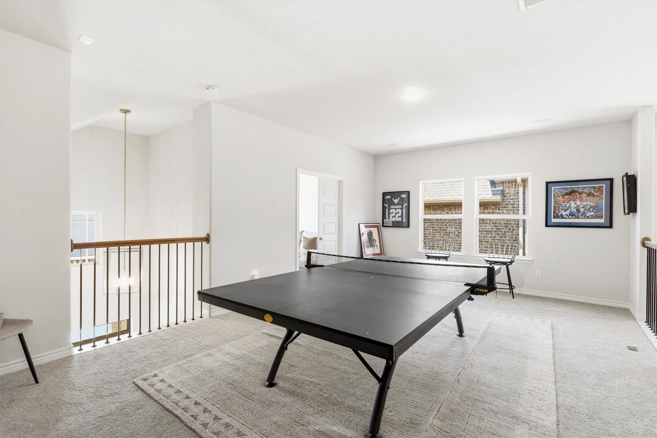 Spacious second-story landing featuring soft carpeting, a wrought iron and wood railing, and two large windows providing natural light