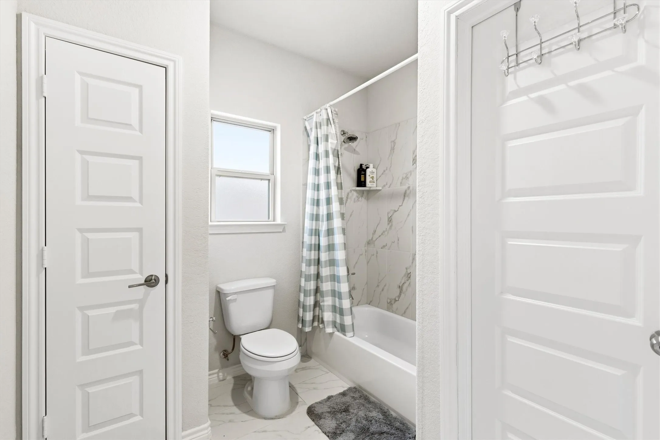 Bright bathroom featuring a white porcelain toilet, a window with frosted lower pane, and a white bathtub with a tile surround and an integrated shelf