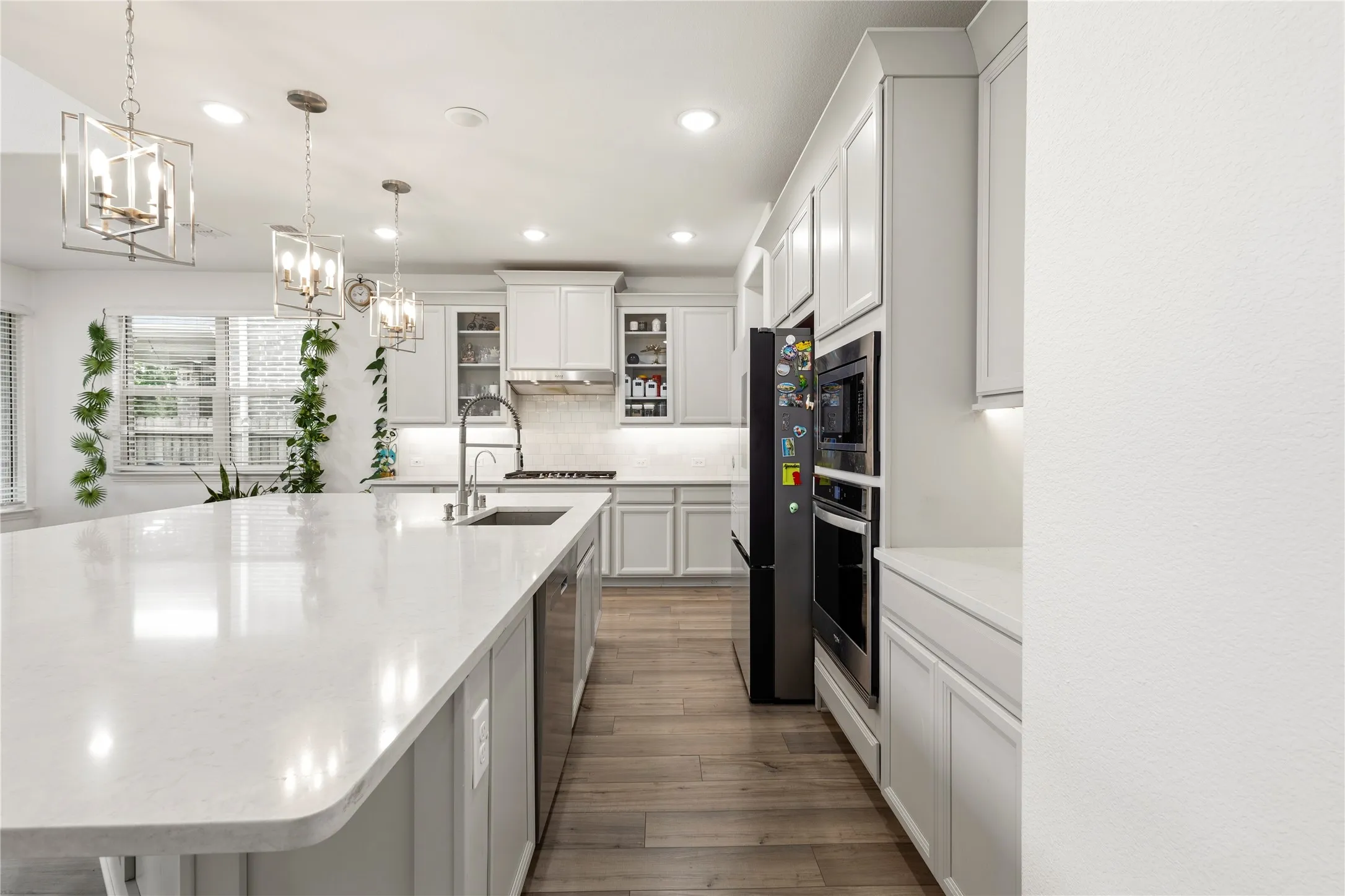 Spacious kitchen featuring a large island with an integrated sink, light-toned cabinetry, wood-finish flooring, recessed lighting, and stainless steel appliances