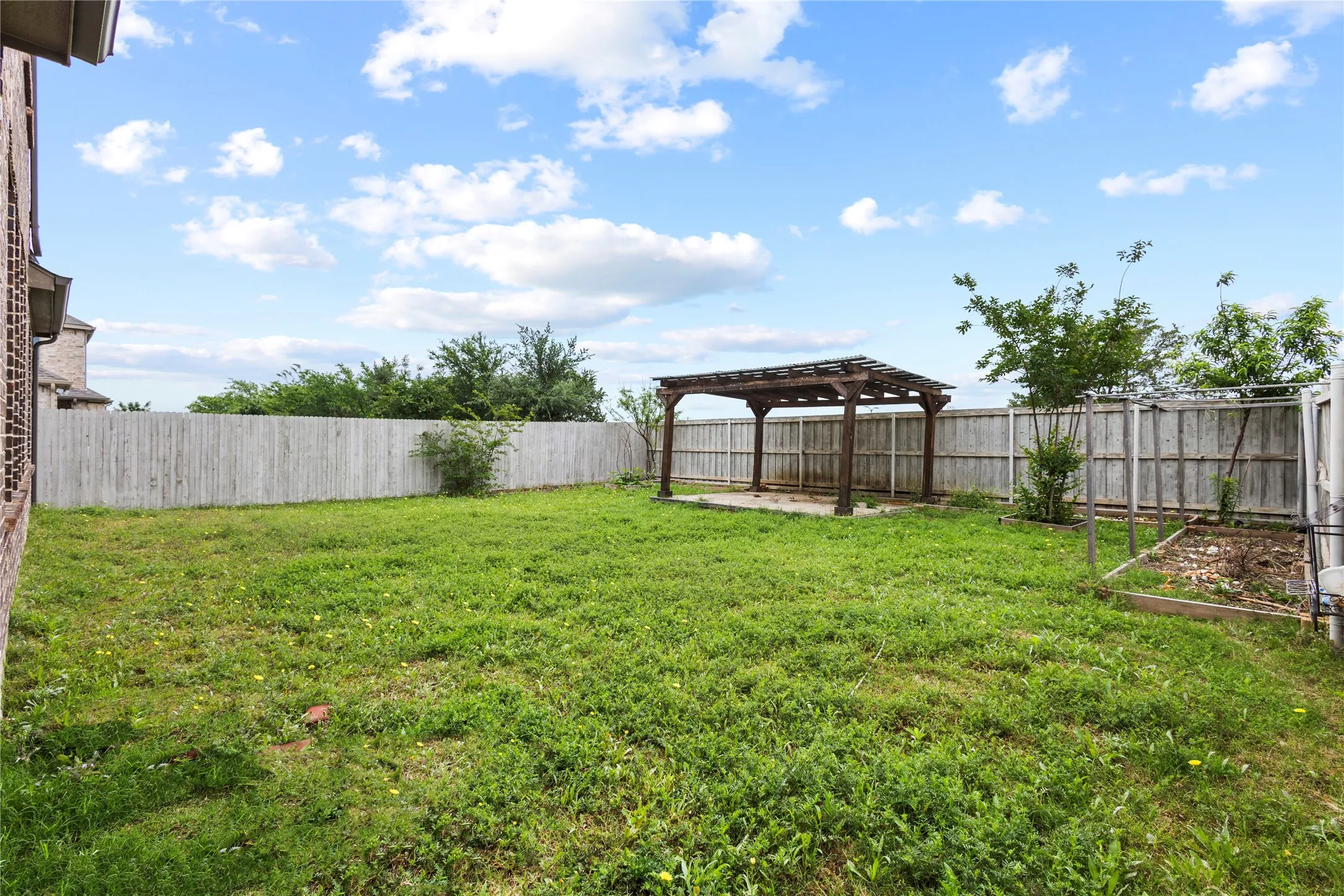 Expansive backyard featuring a large wooden pergola over a concrete pad, surrounded by wood privacy fencing