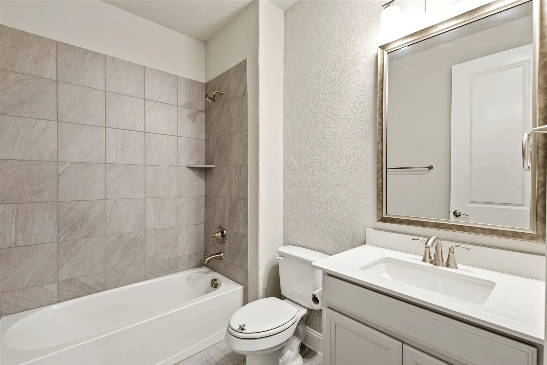 Bathroom featuring a white tub, light gray tile surround, and brushed nickel fixtures