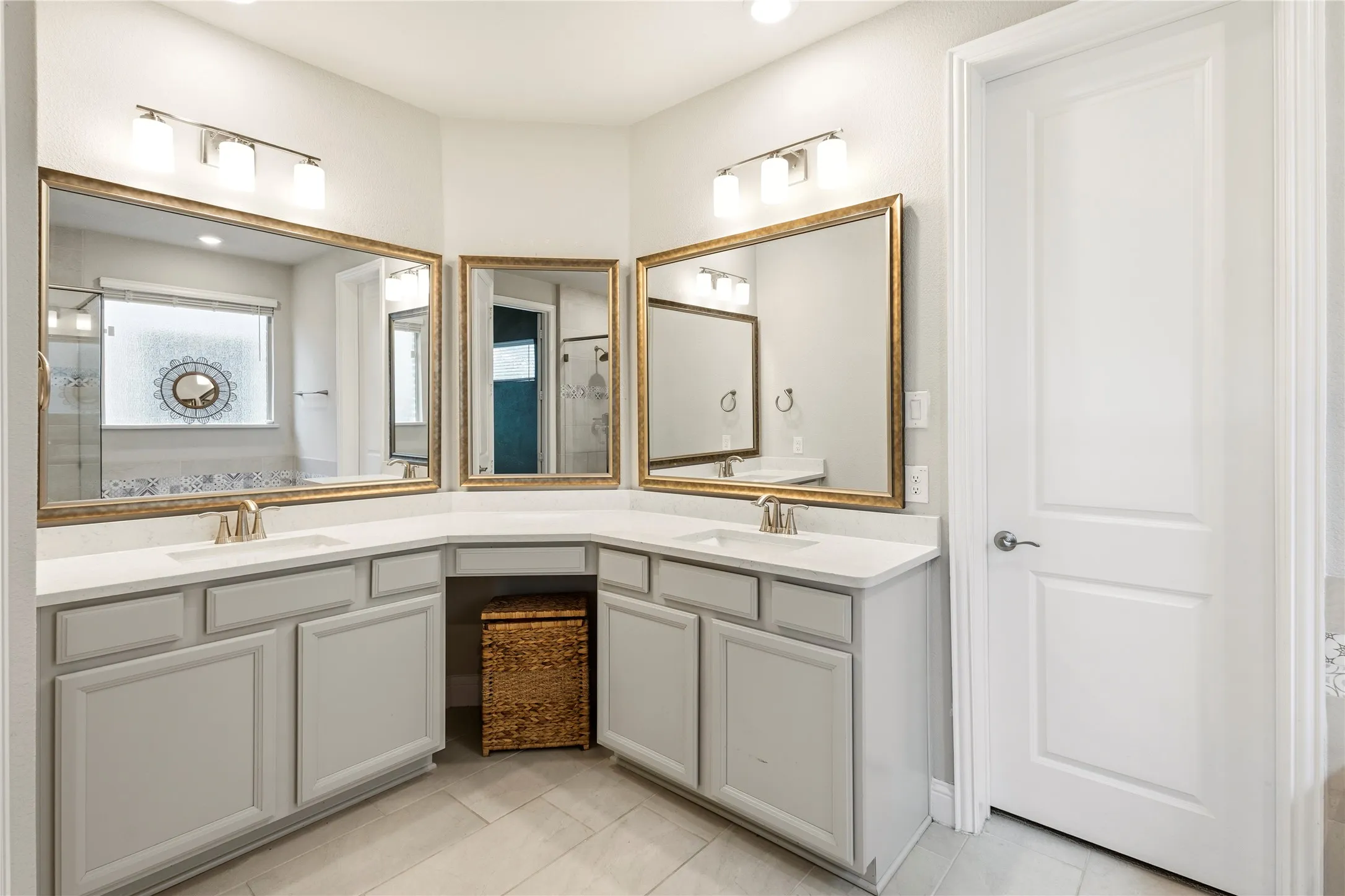 Dual sink vanity with light gray cabinetry, light countertops, and gold-framed mirrors