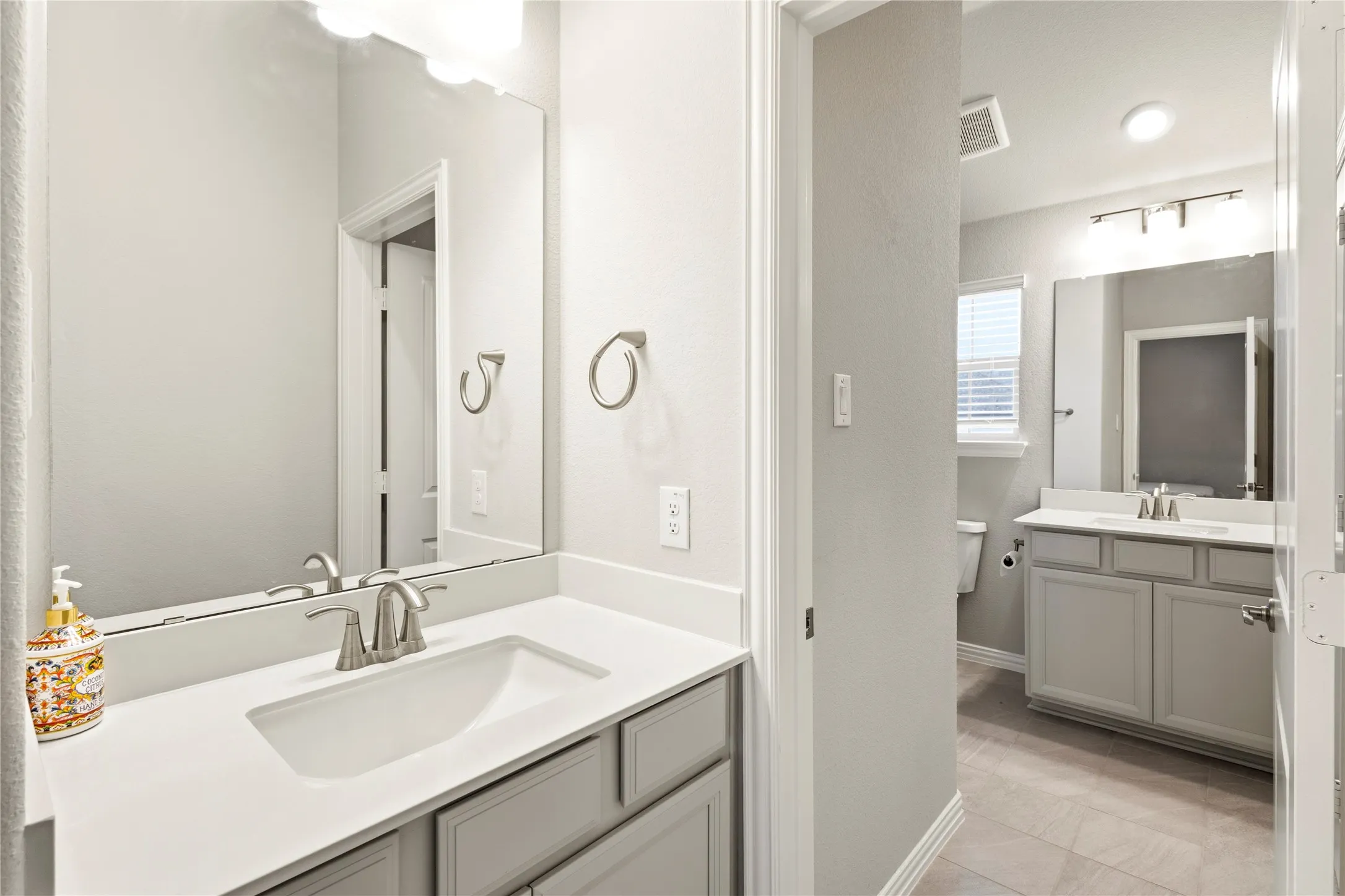 Dual vanity bathroom featuring light gray cabinetry, white countertops, rectangular undermount sinks, and brushed nickel fixtures