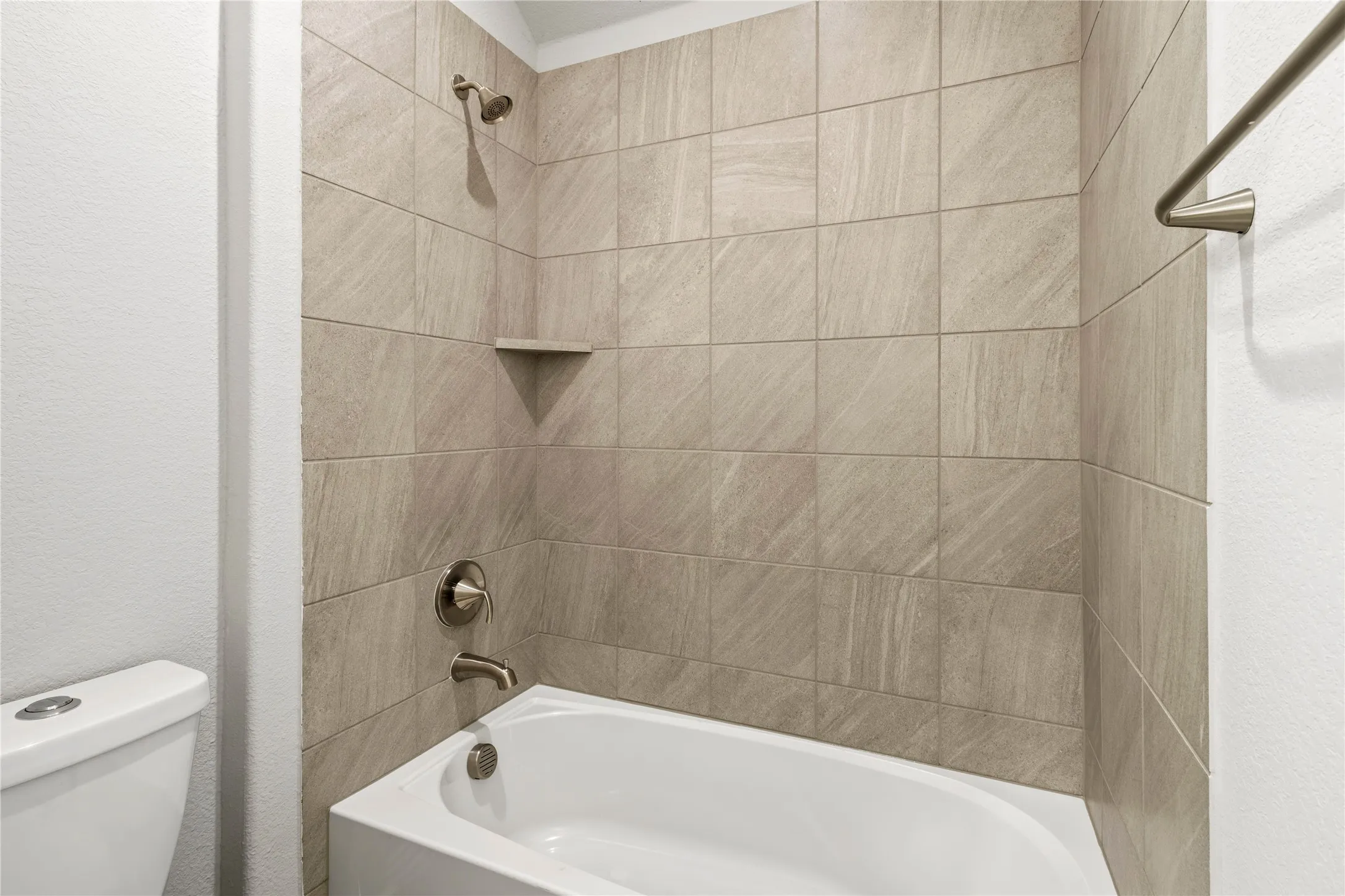 Tub and shower combination featuring neutral-toned tile surround, brushed nickel fixtures, and an integrated corner shelf