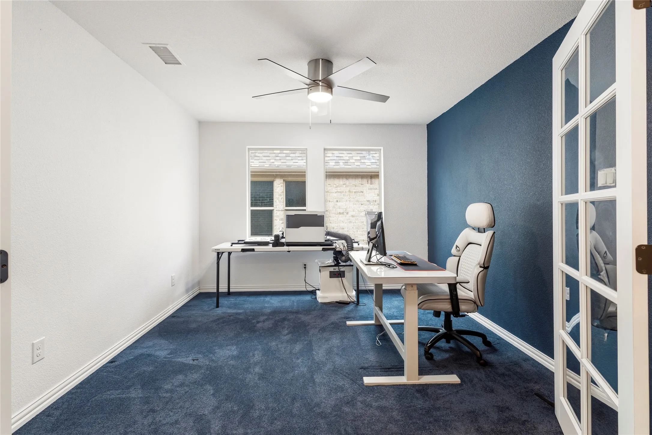 Private room featuring a deep blue accent wall, blue carpet flooring, and two windows providing natural light