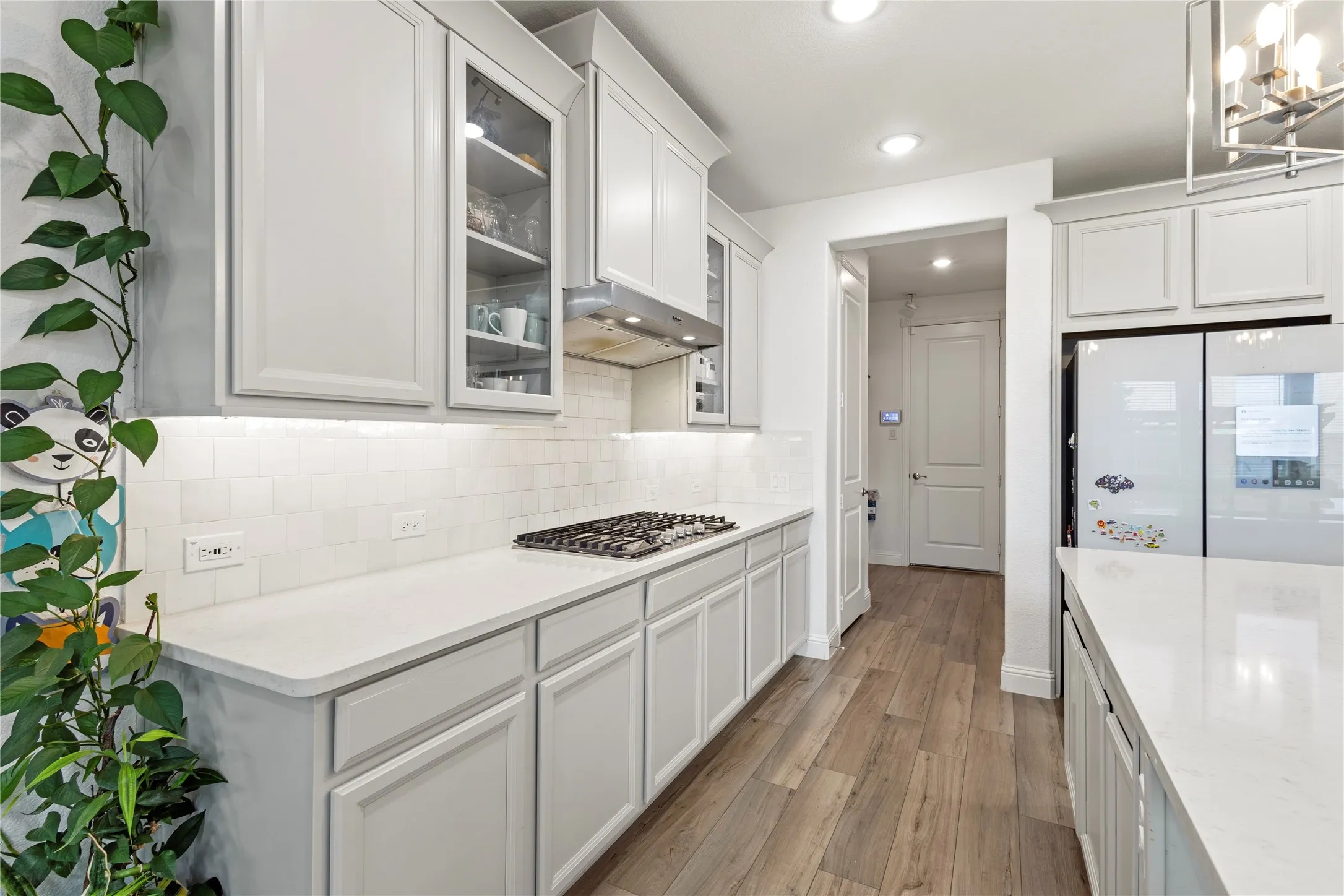 Contemporary kitchen featuring wood-finish flooring, white cabinetry, integrated range with overhead ventilation, undermount lighting, and a subway tile backsplash