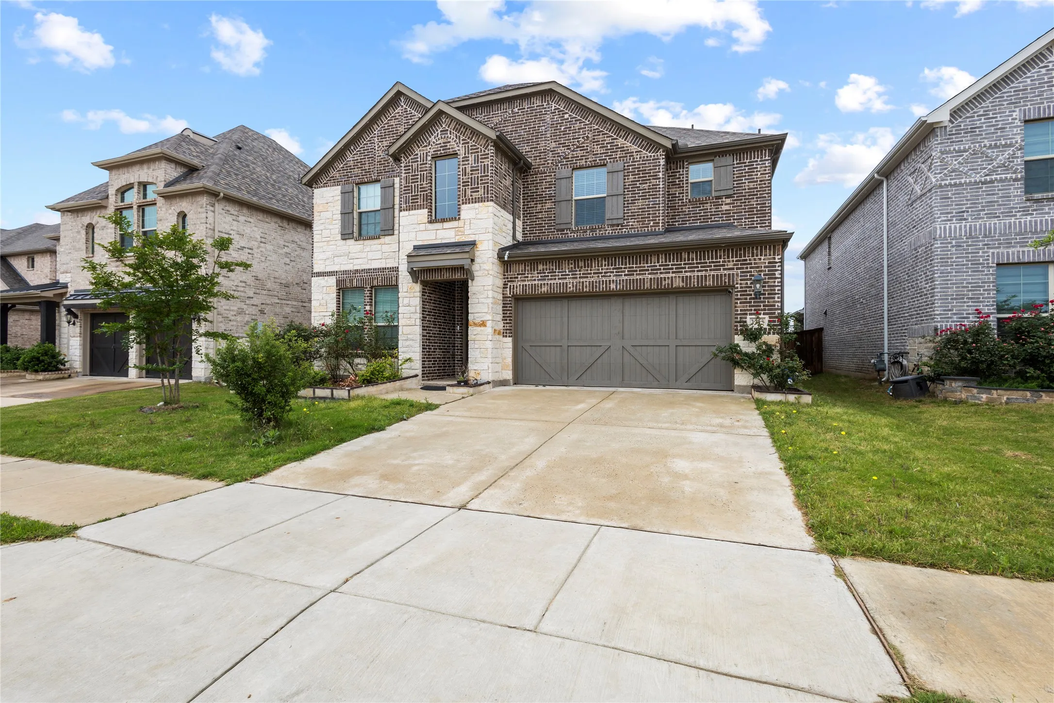 Two-story exterior featuring a brick and stone facade, a two-car garage with an overhead door, and a concrete driveway