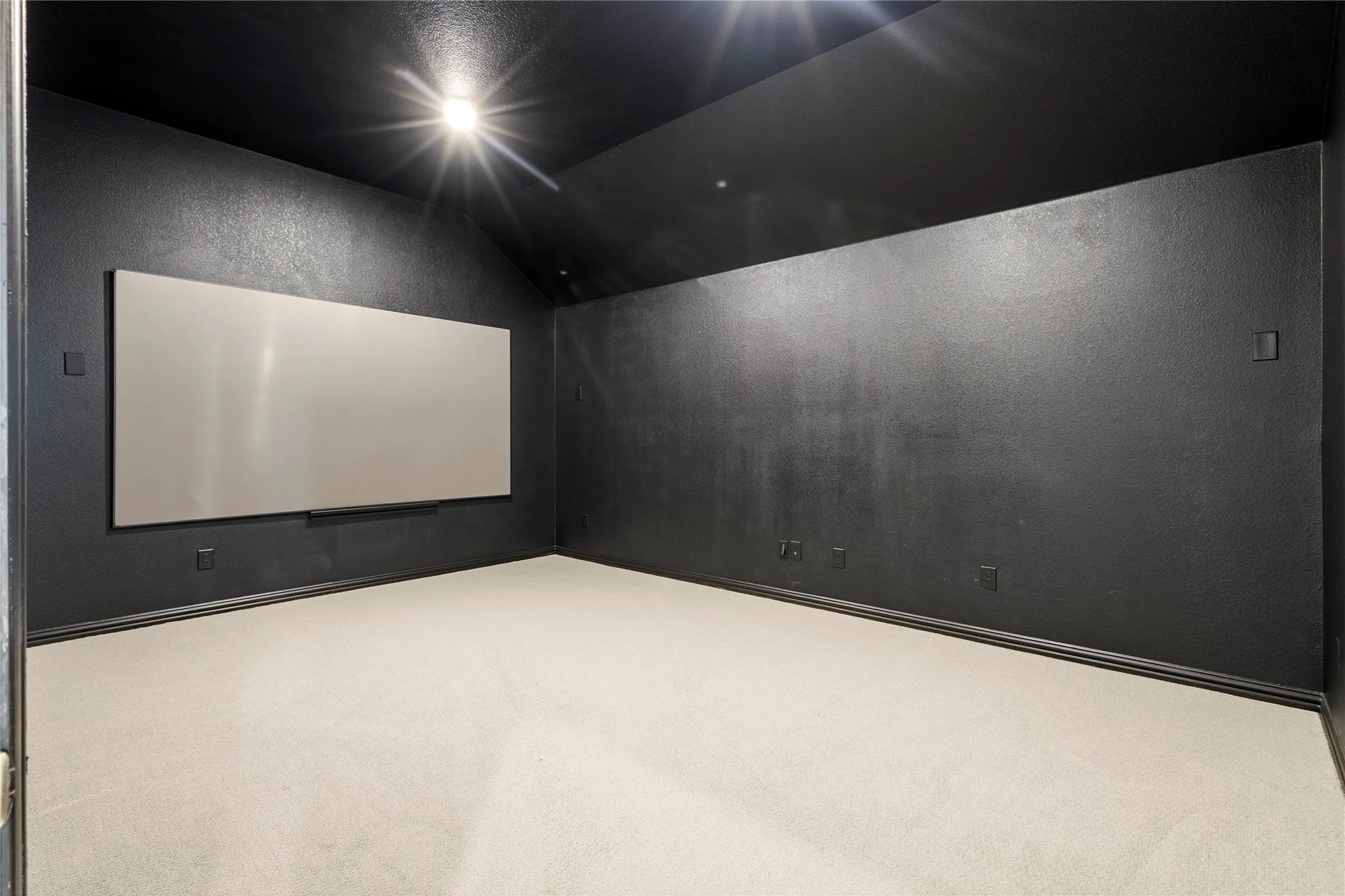 Dedicated media room featuring a large projection screen, dark painted walls, a vaulted ceiling, recessed lighting, and light-colored carpeting