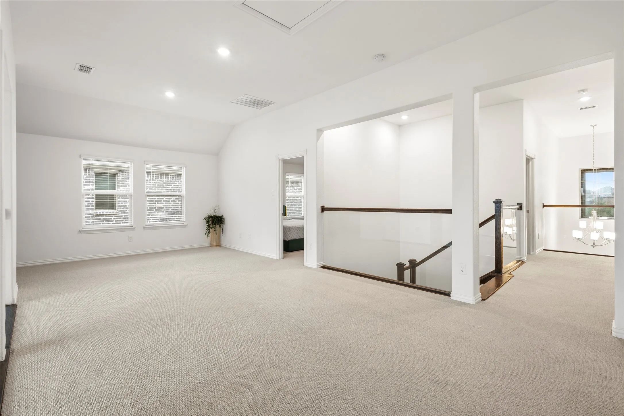 Expansive carpeted loft space featuring double windows with blinds, recessed lighting, and a glass-paneled railing overlooking the stairwell