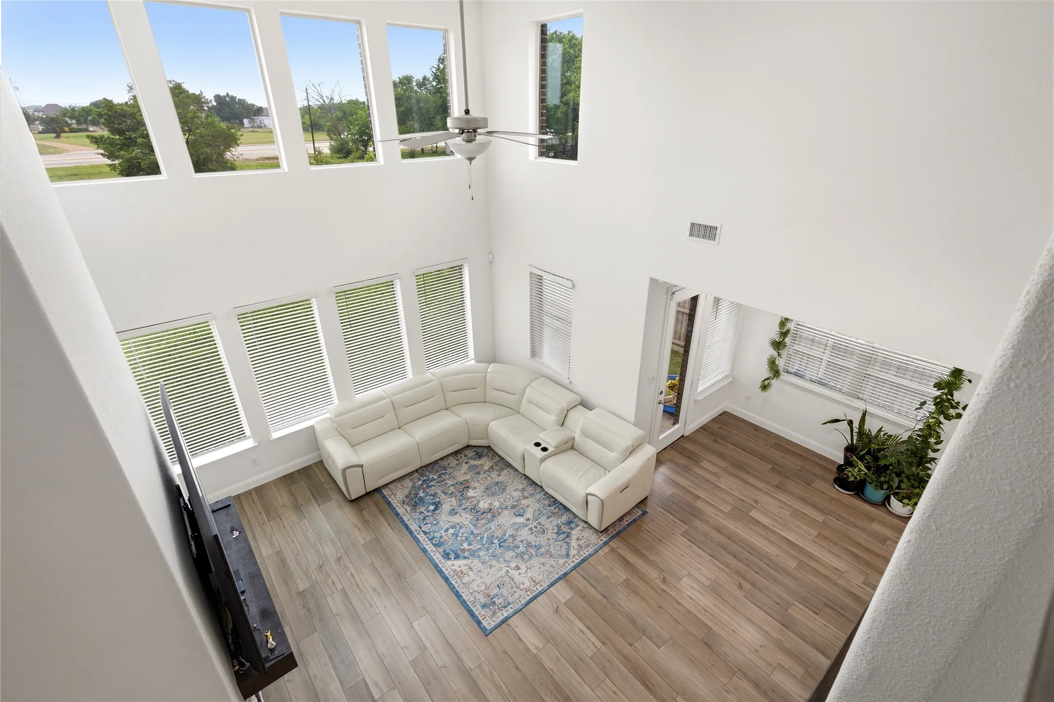 Two-story living area featuring a vaulted ceiling with a ceiling fan, wood-finish flooring, and multiple large windows