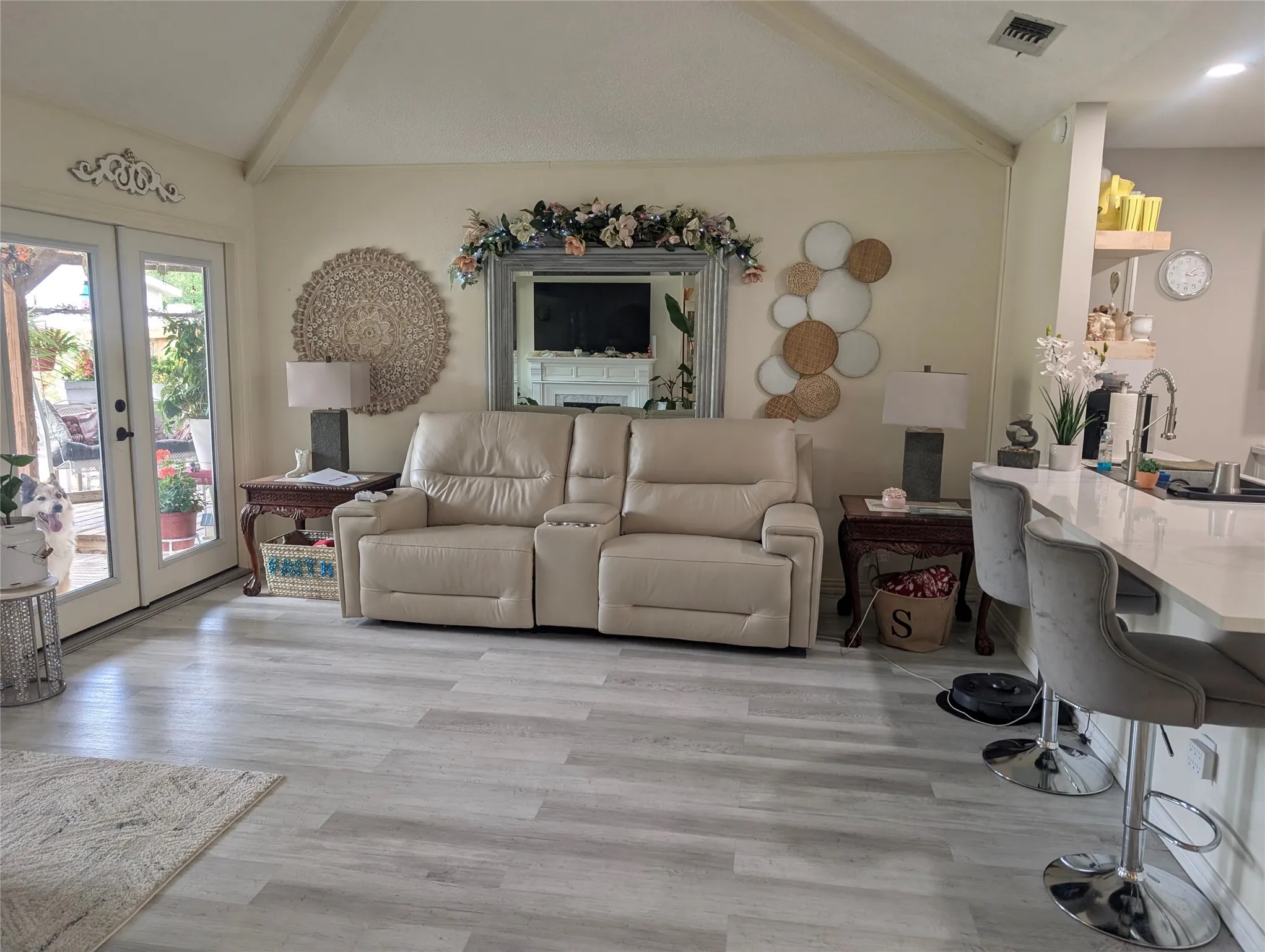 Open living space approx 19x19 with gray laminate floors and natural light. Notice the double doors leading outside or the granite bar