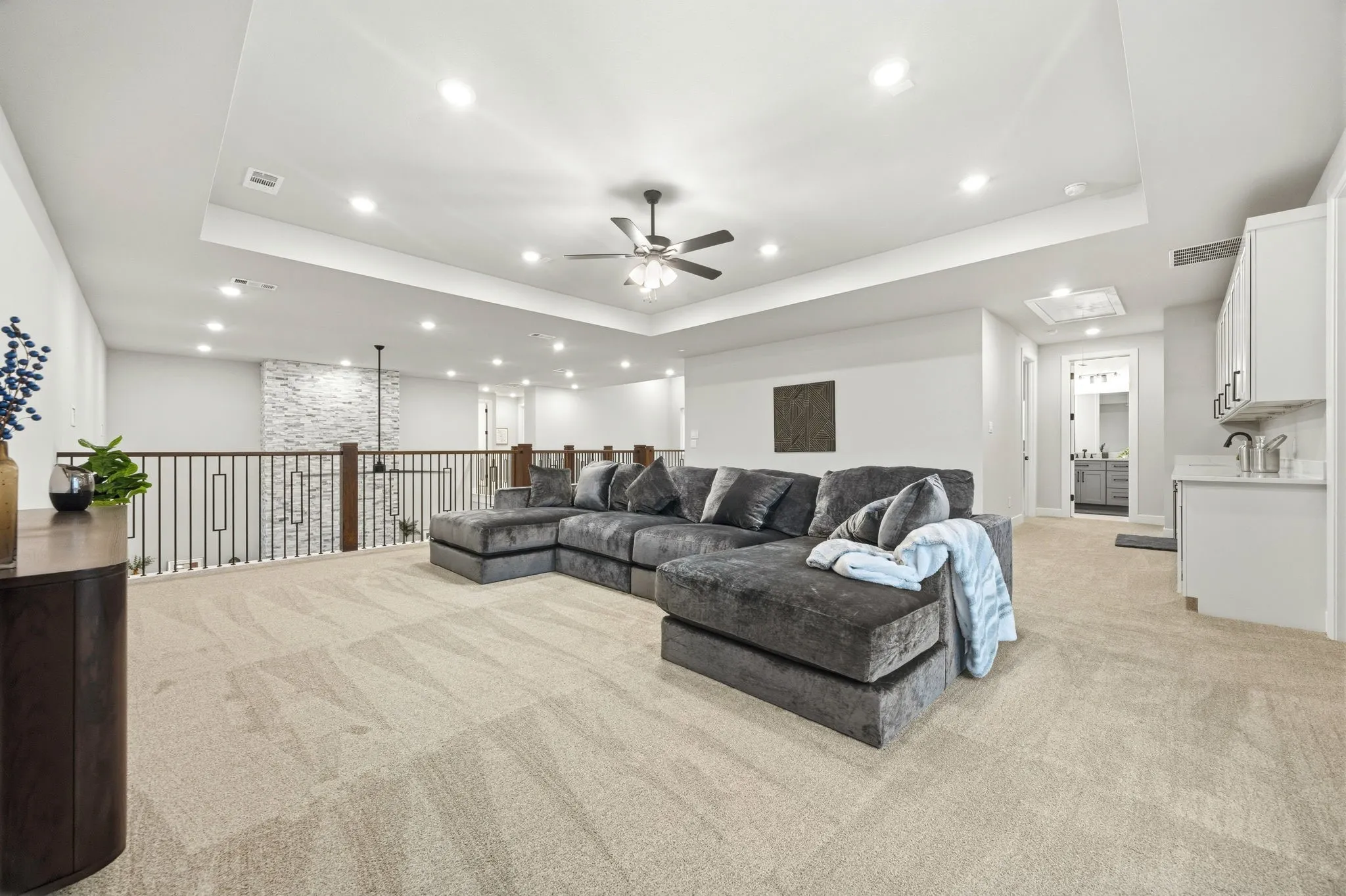 Spacious loft area featuring light carpet flooring, a tray ceiling with recessed lighting, and a ceiling fan